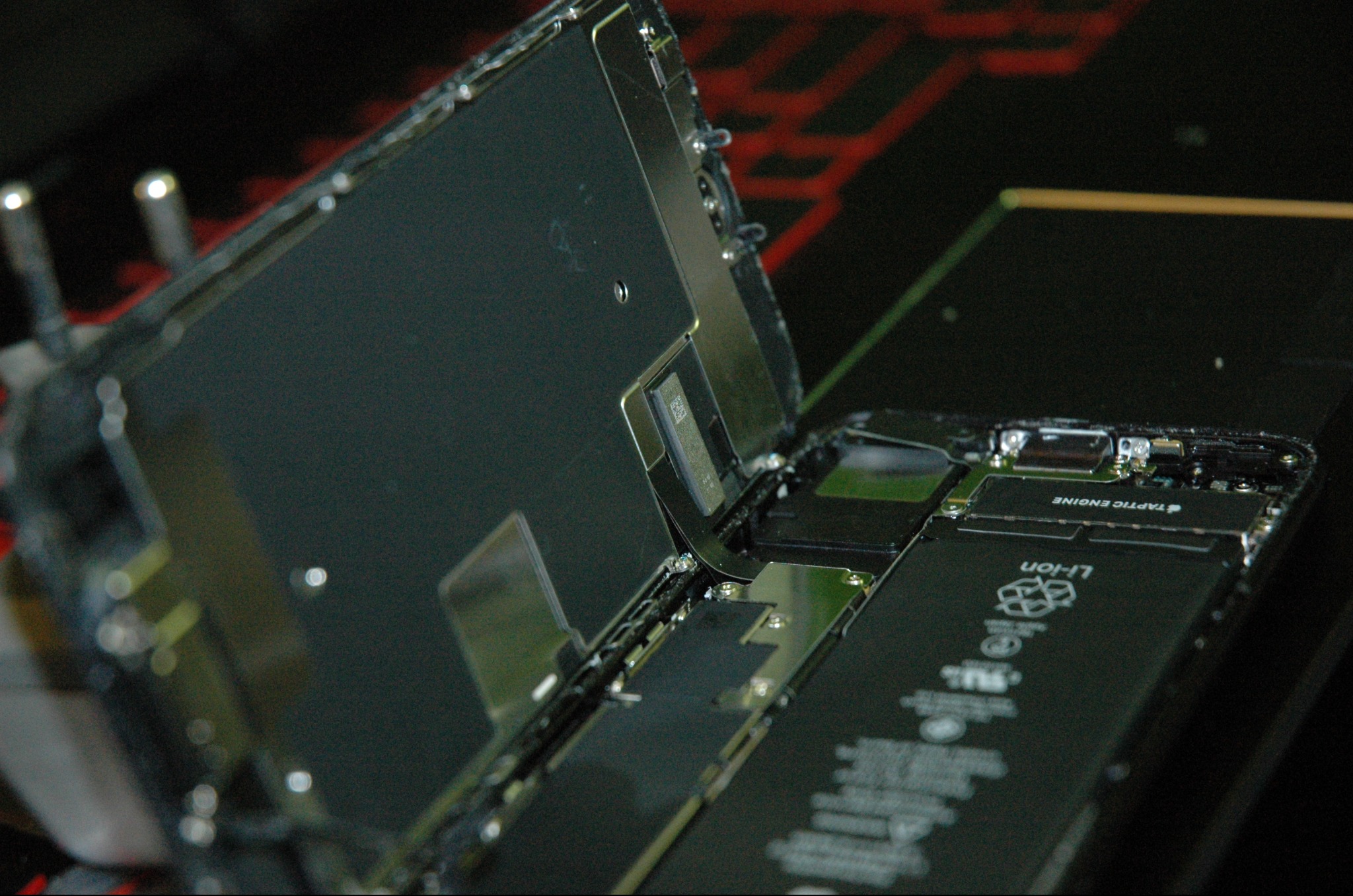 Otwarty iPhone podczas naprawy; widoczna bateria Li-ion, Taptic Engine i wewnętrzne komponenty elektroniczne.