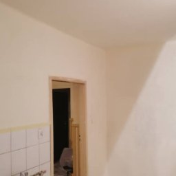 TSiD-tanio, szybko i dokladnie - Świeżo pomalowane na kremowo ściany i sufit w trakcie remontu, widoczne ślady po remoncie w kuchni i na podłodze, niezabezpieczone rury w kuchni, surowe futryny drzwiowe.