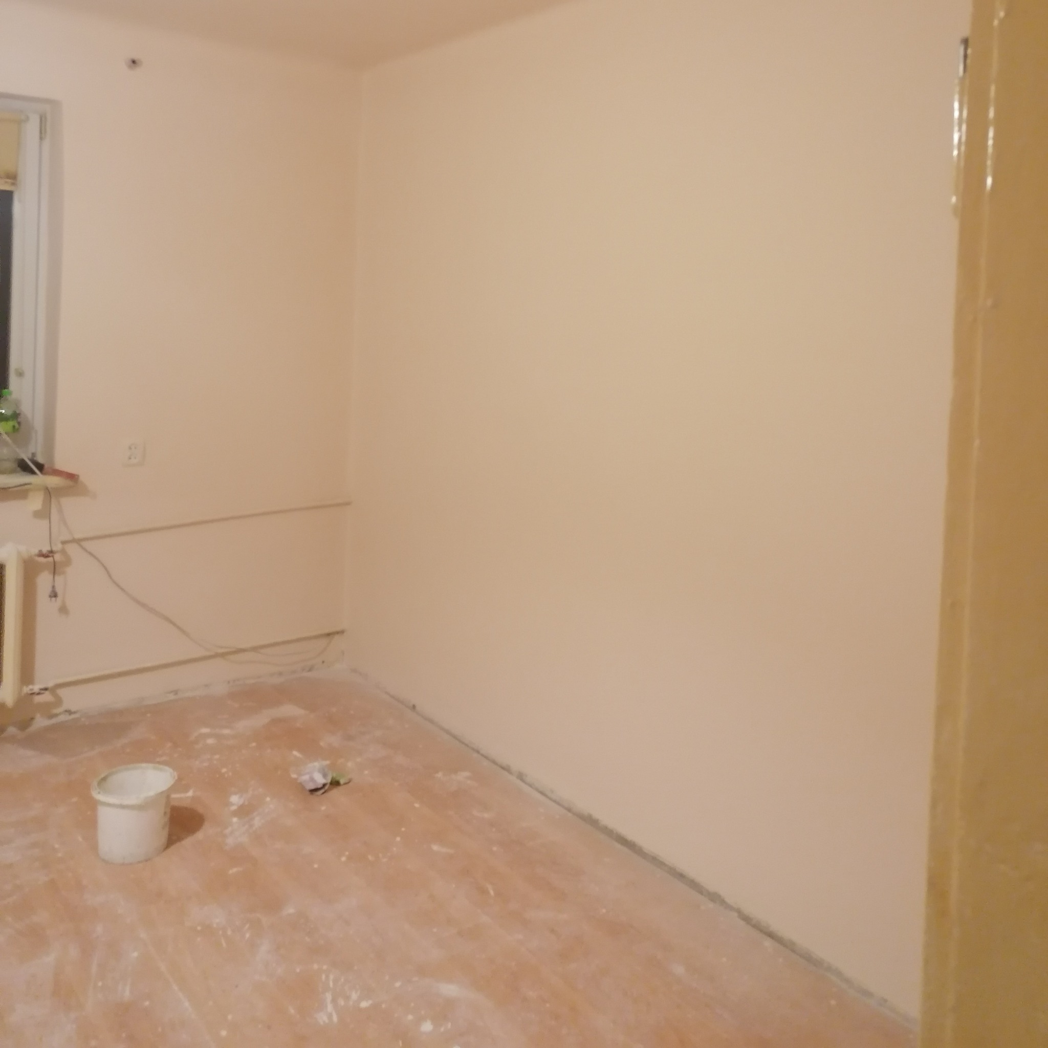 Pomieszczenie po malowaniu ścian na jasny odcień, widoczny kubeł po farbie i zabrudzenia na podłodze.