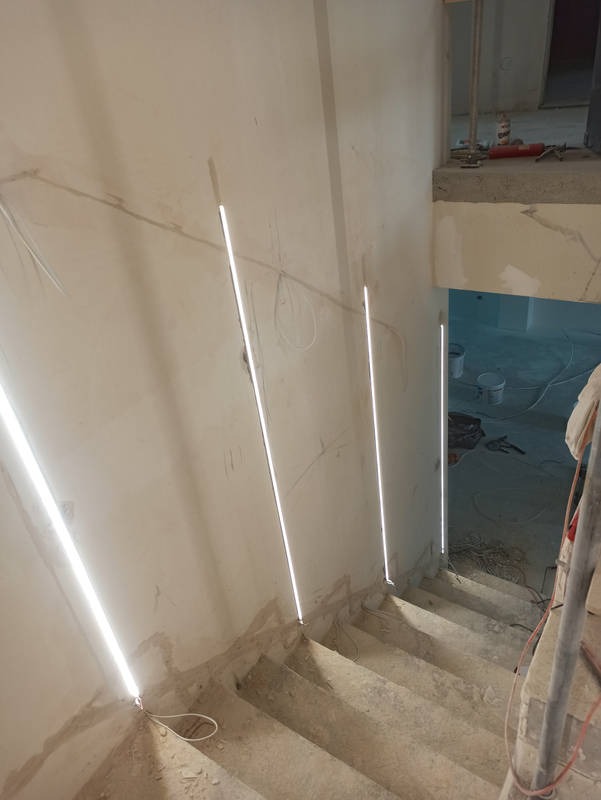 Montaż oświetlenia LED w pionowych szczelinach wzdłuż schodów, widoczne przewody, surowy stan ścian i schodów przed wykończeniem.