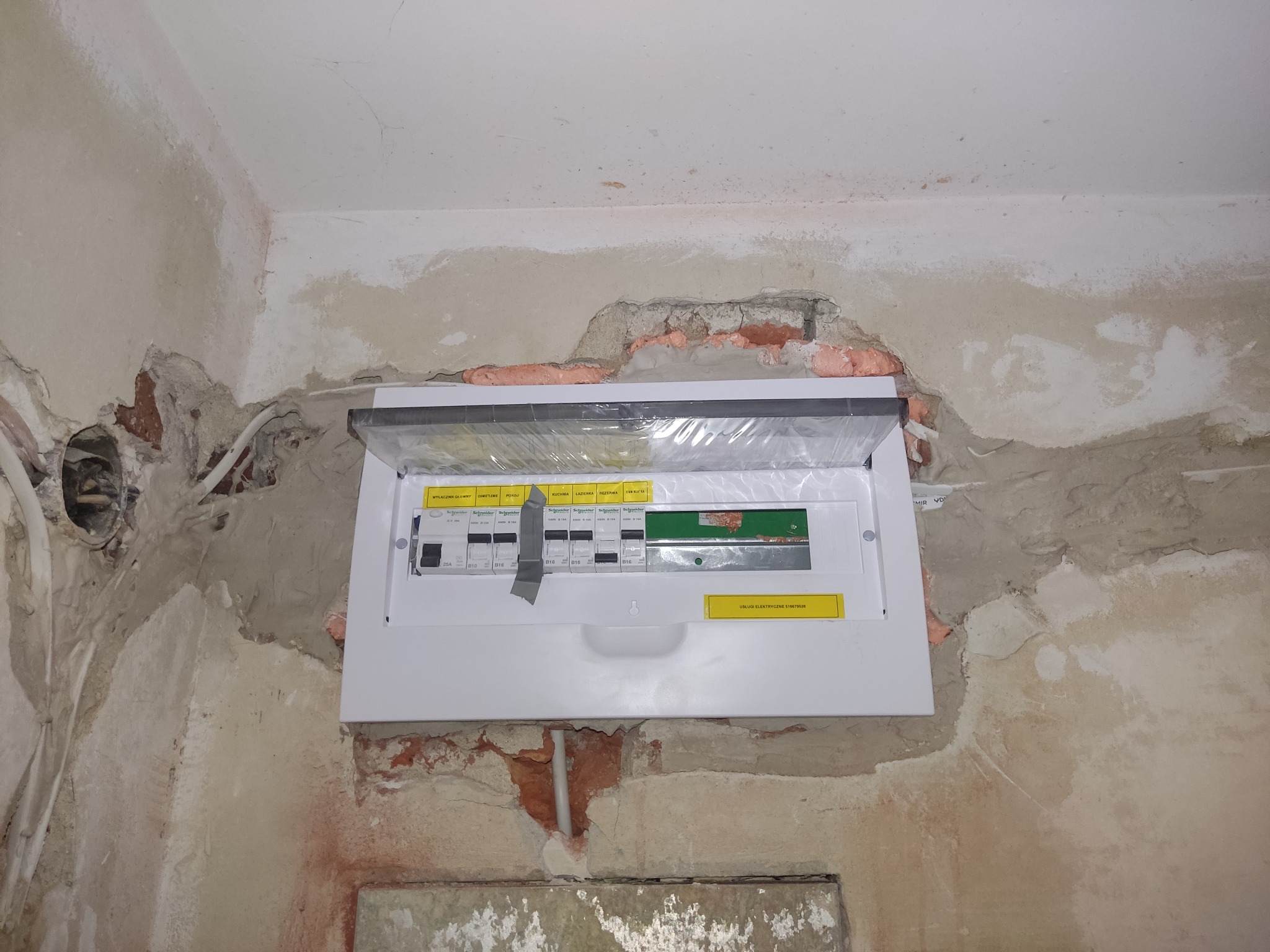 Nowa skrzynka bezpiecznikowa zamontowana w ścianie w trakcie remontu, widoczne ślady po kuciu i instalacji przewodów.
