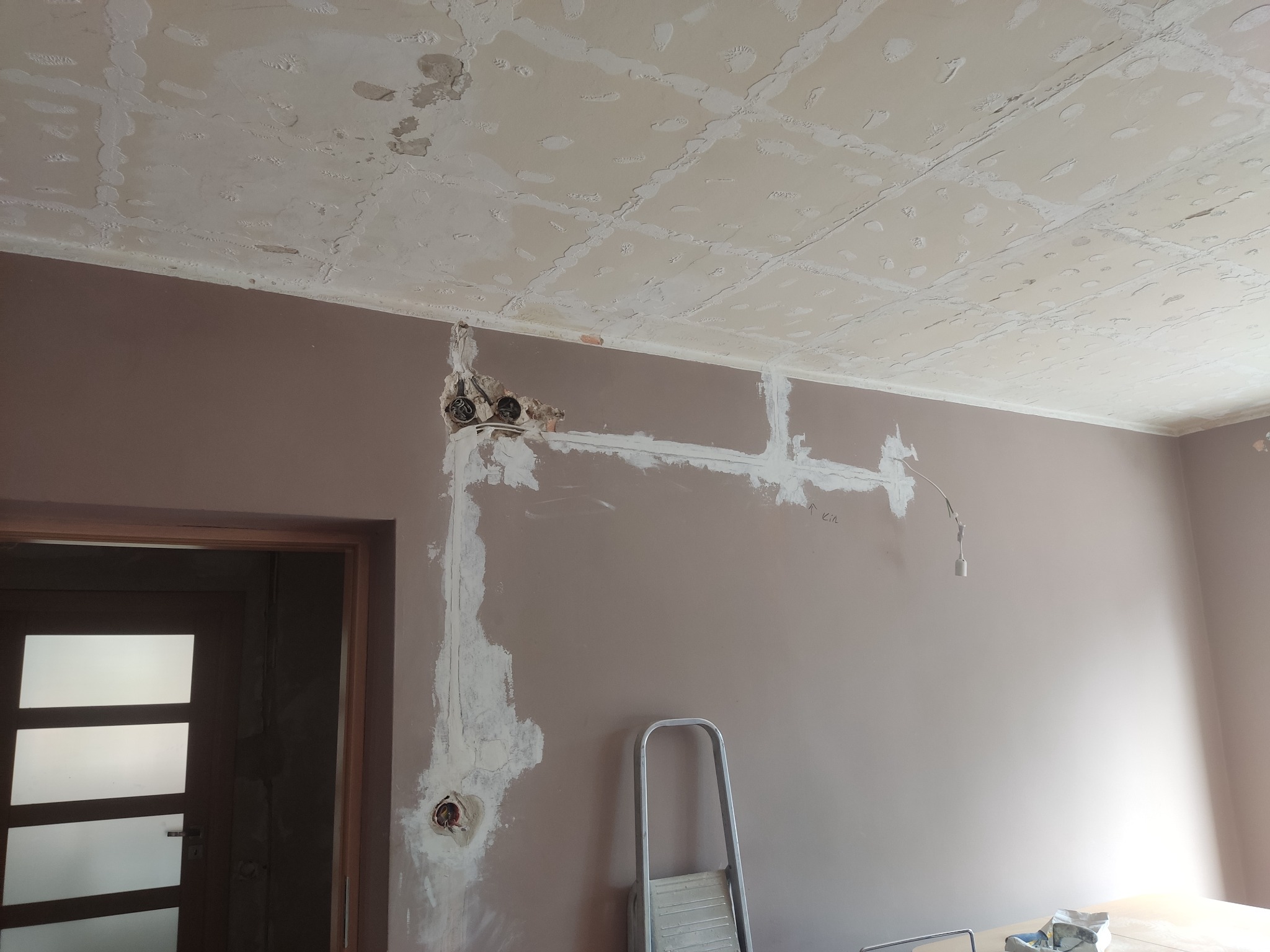Przygotowanie ścian do malowania: widoczne puszki elektryczne, bruzdy po przewodach zalane gipsem, sufit po szpachlowaniu, drabina aluminiowa oparta o ścianę.