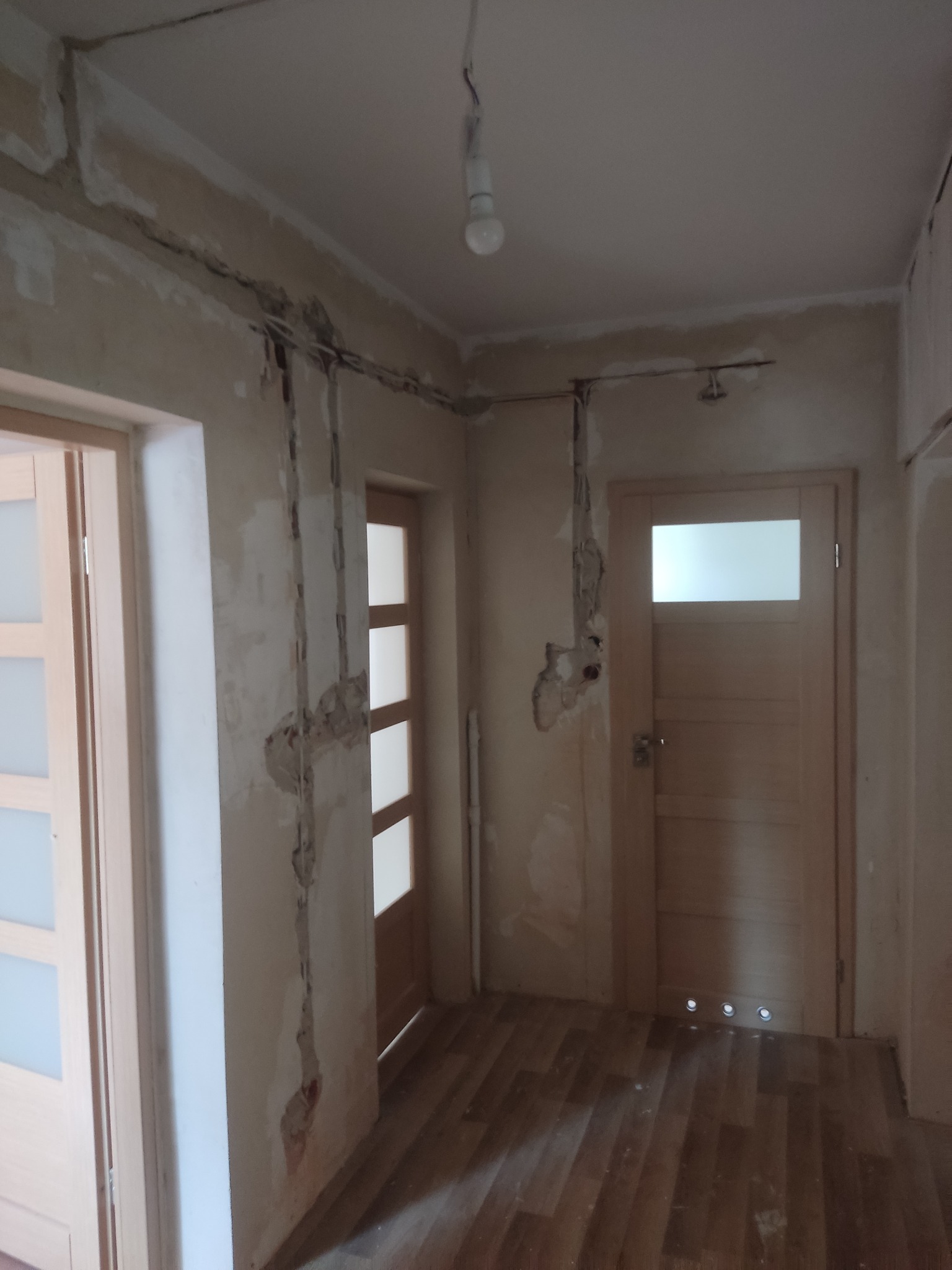 Wnętrze mieszkania w trakcie remontu: widoczne kable elektryczne wystające ze ścian, przygotowane pod instalację, oraz fragmenty uszkodzonego tynku.