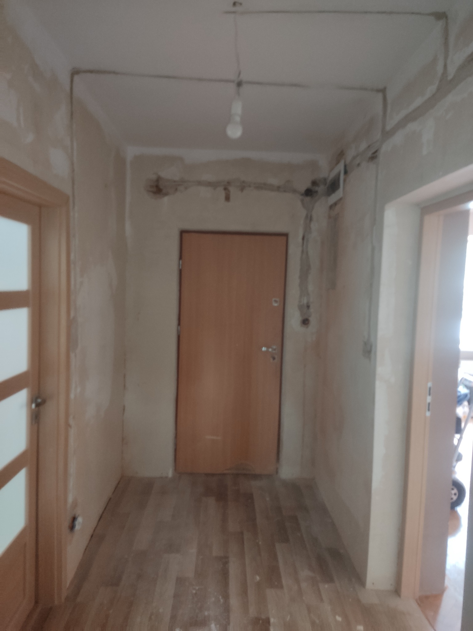 Korytarz w trakcie remontu, widoczne kable elektryczne poprowadzone po ścianach i suficie, przygotowane do montażu gniazd i włączników, ściany w stanie surowym przed malowaniem, podwieszona żarówka.