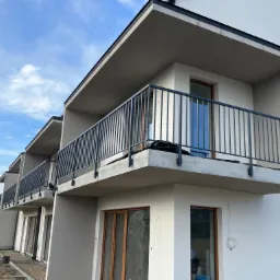 Nowoczesne balkony z ciemnymi, metalowymi balustradami w nowo wybudowanym domu wielorodzinnym, widoczne ślady prac wykończeniowych na zewnątrz budynku.