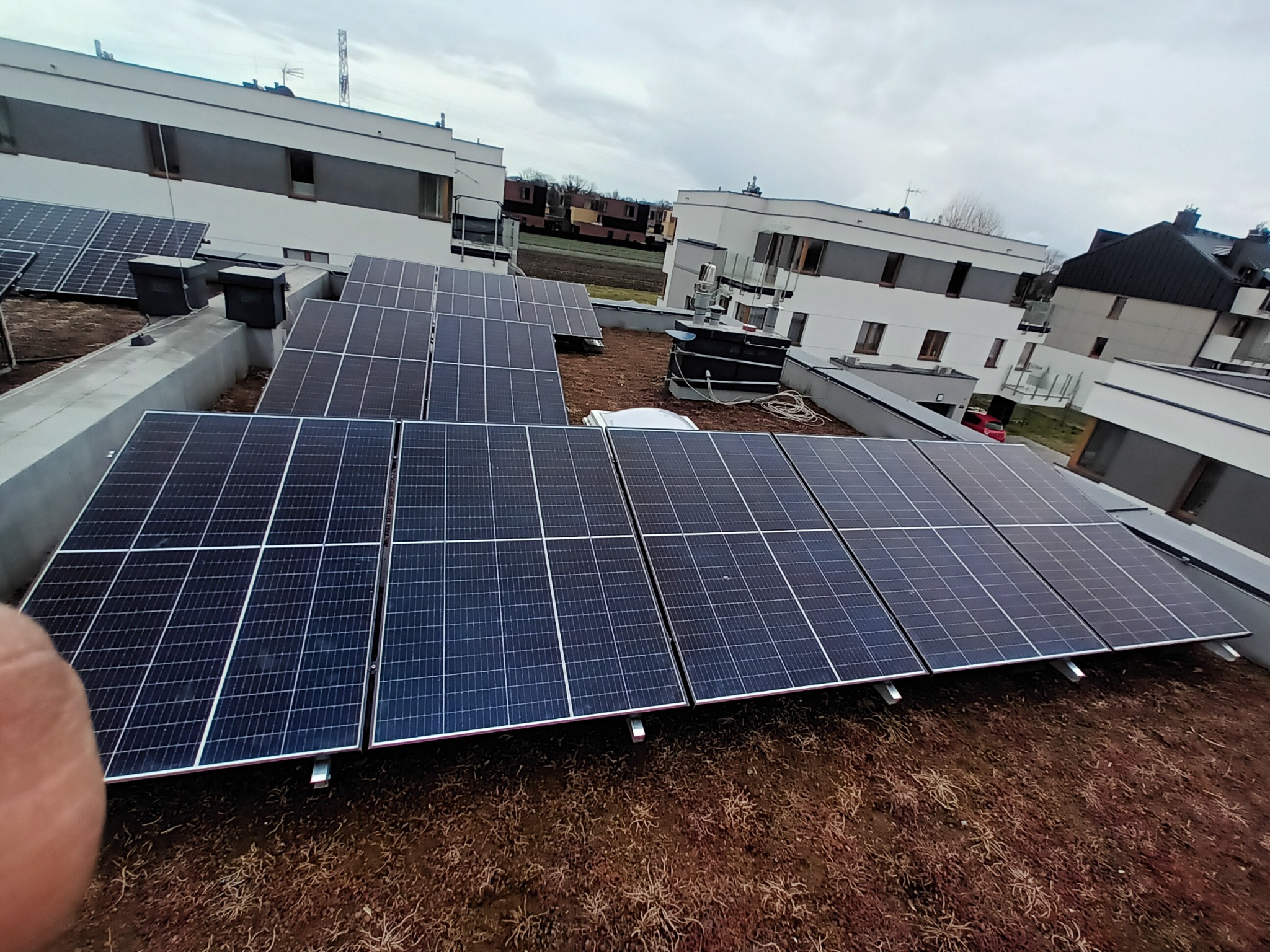 Panele słoneczne na zielonym dachu budynku mieszkalnego, widok z góry, pochmurne niebo.