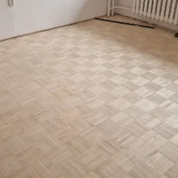Parkiet ułożony w kwadraty, widoczne ślady po listwach przypodłogowych, przygotowany do dalszych prac wykończeniowych.