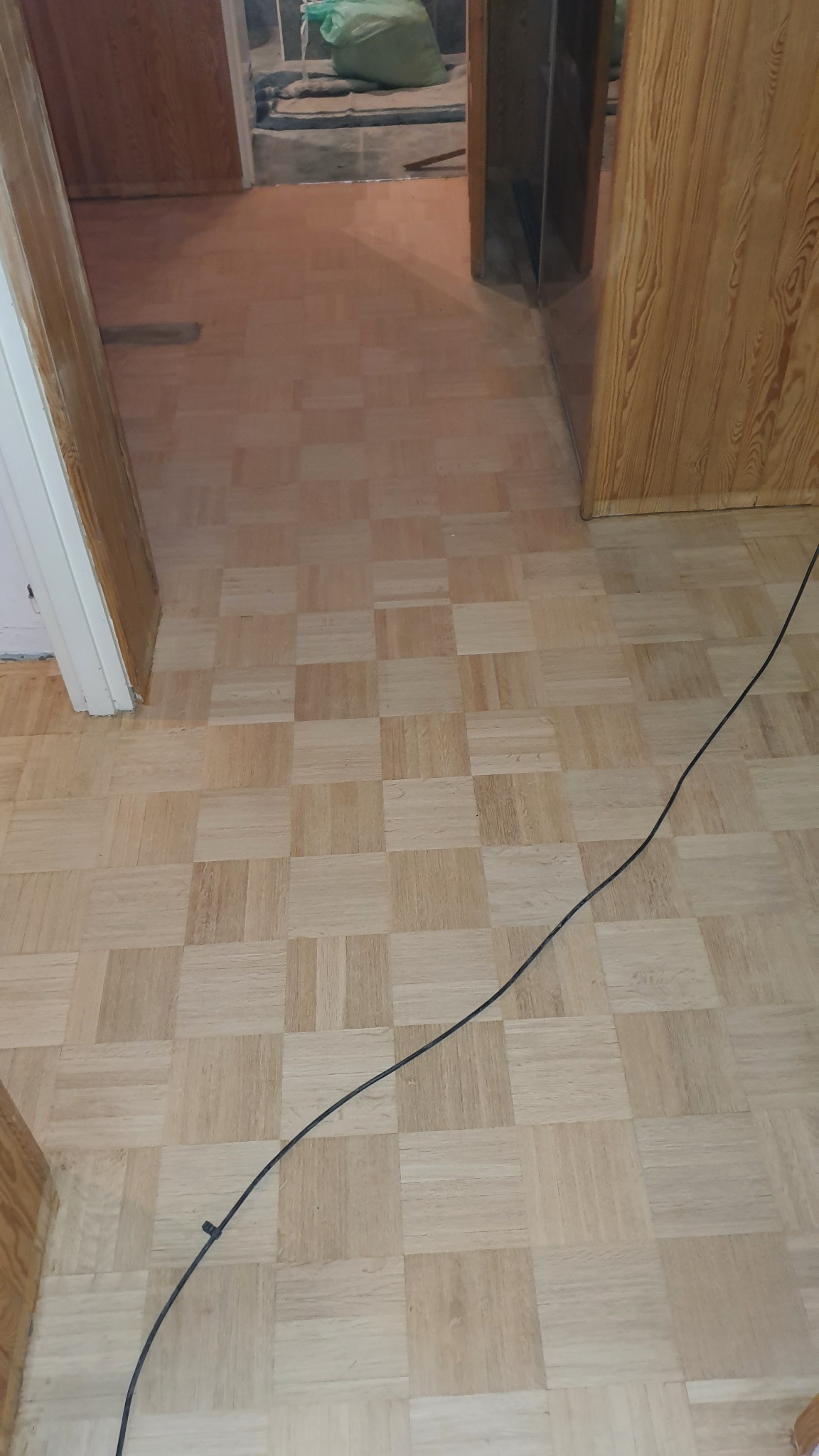 Parkiet ułożony w kwadraty, widoczny kabel elektryczny na podłodze, remont w tle.