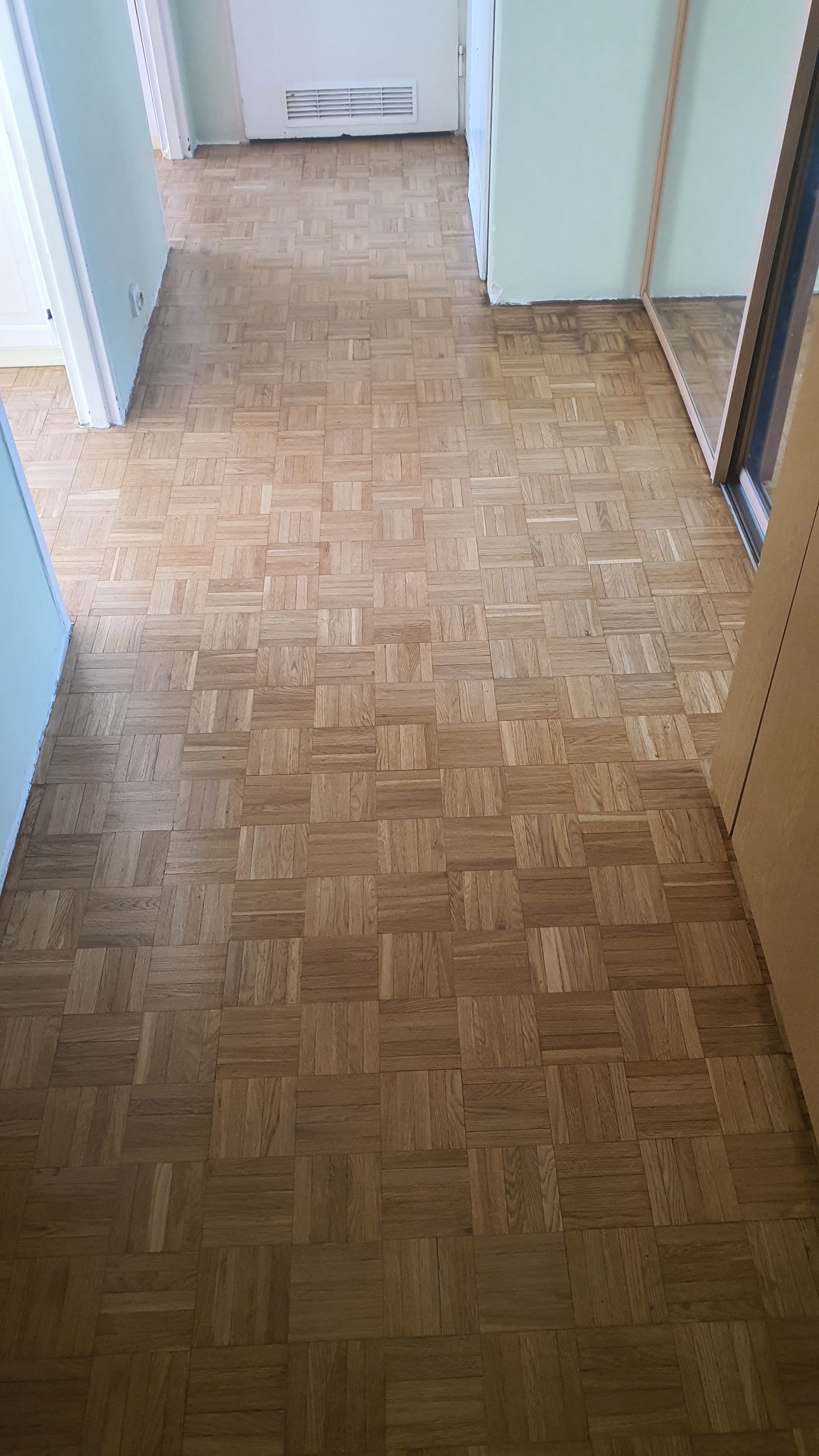 Parkiet ułożony w kwadraty, widoczny w korytarzu mieszkania, po renowacji. Widoczne ślady po szlifowaniu w niektórych miejscach.