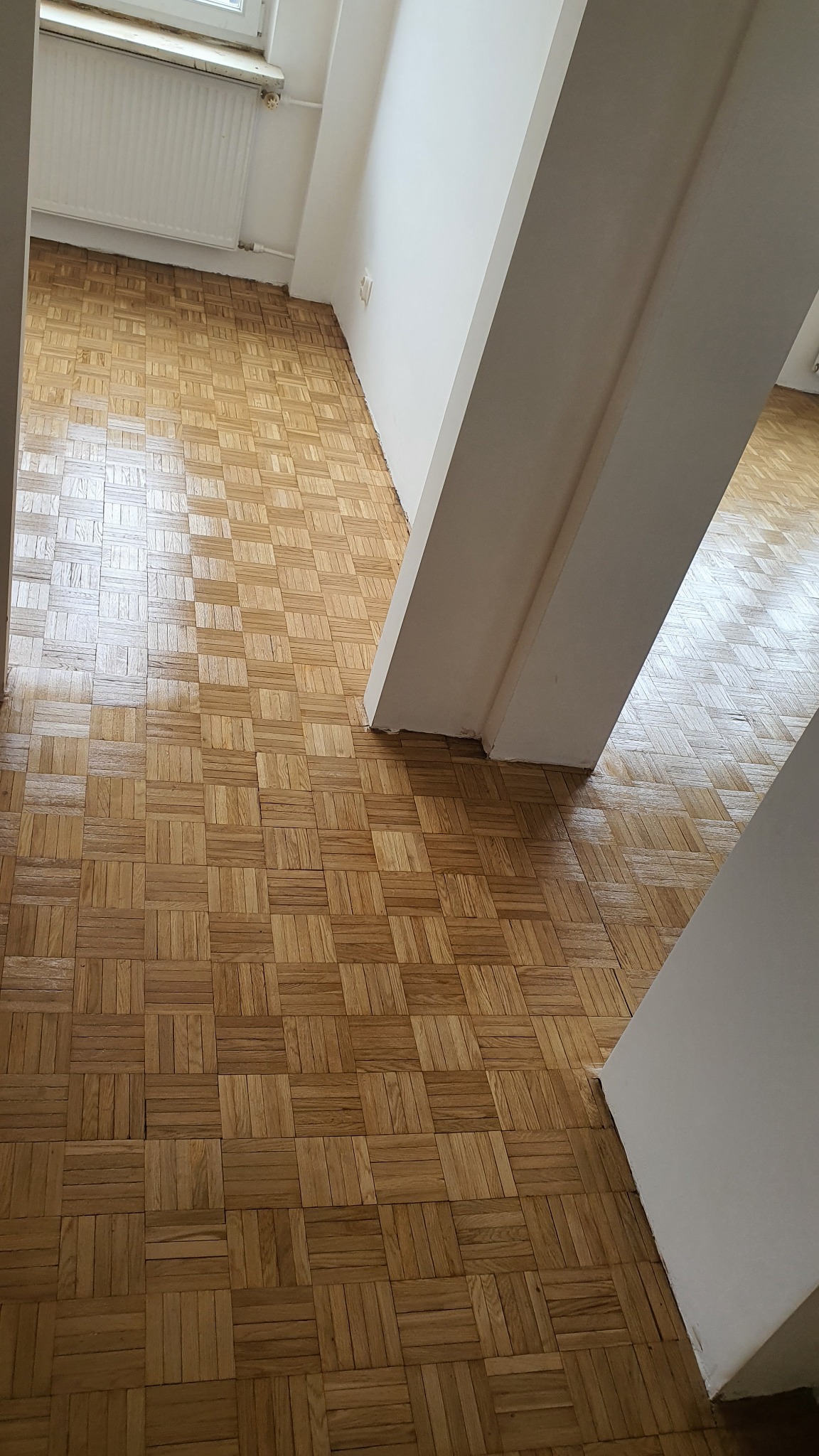 Parkiet ułożony w jodełkę po renowacji, widoczne odświeżone drewno i fragment ściany z filarem.