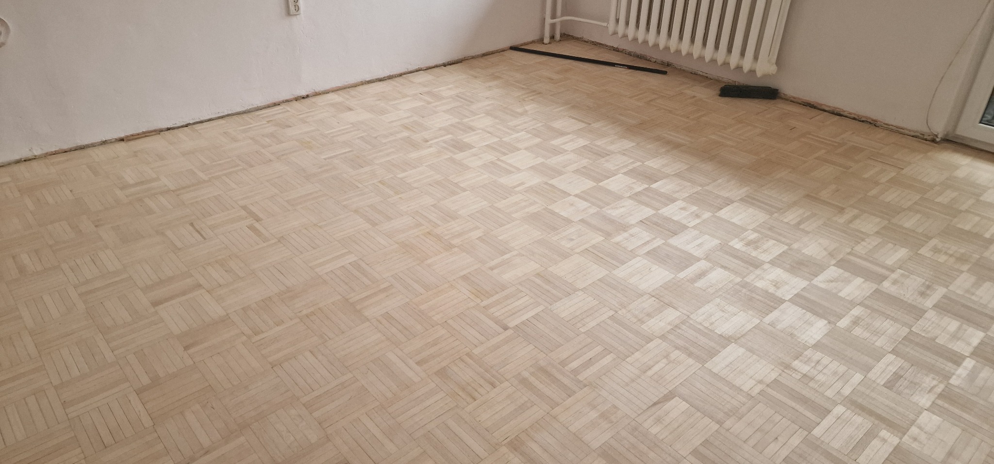 Parkiet ułożony w kwadraty, widoczne ślady po listwach przypodłogowych, przygotowany do dalszych prac wykończeniowych.