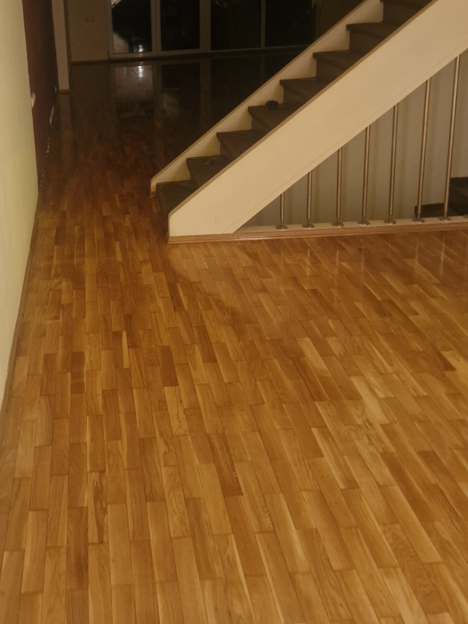 Wycyklinowana, lakierowana podłoga parkietowa z drewna dębowego w pomieszczeniu z białymi schodami o metalowych barierkach.