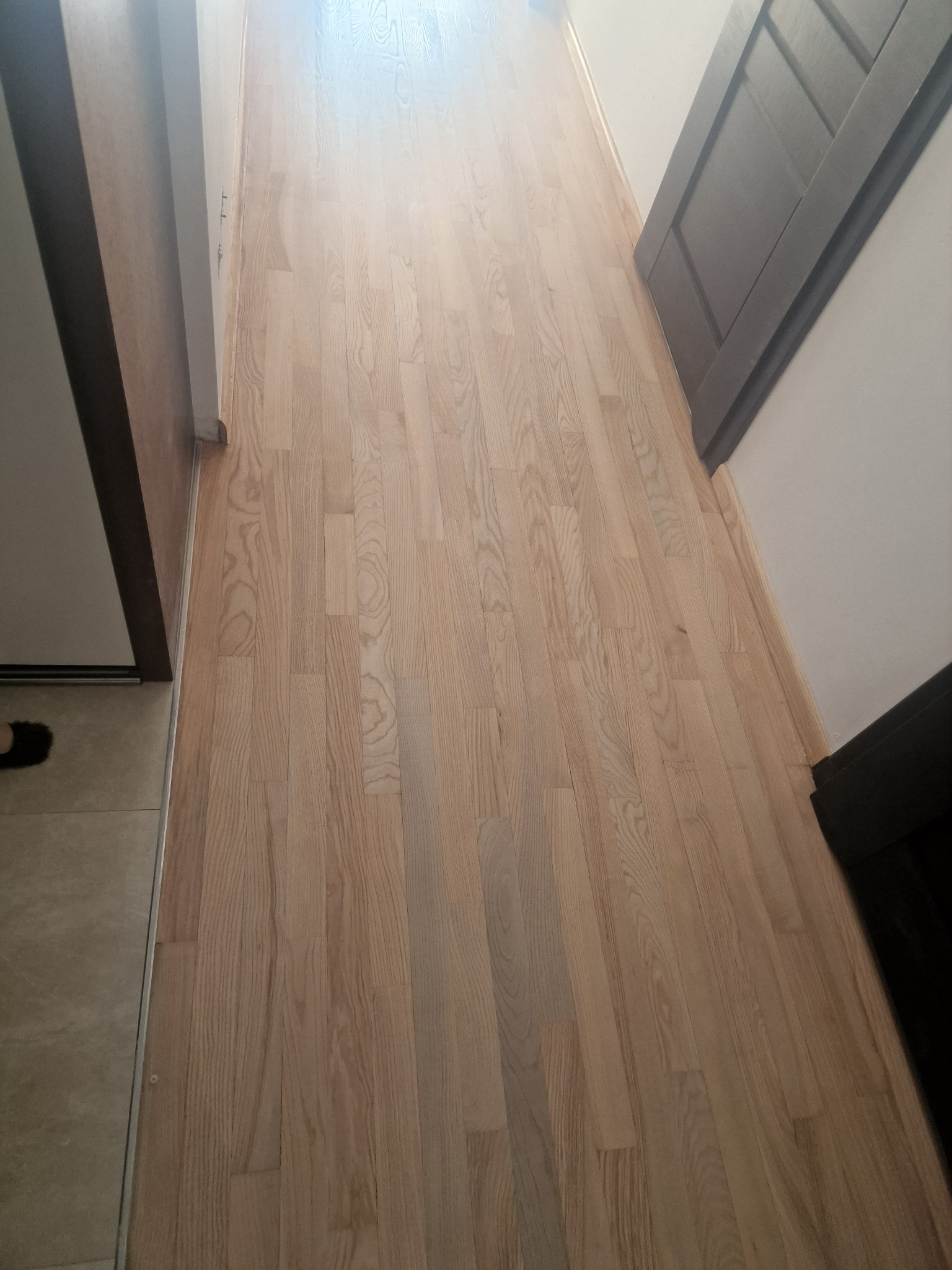 Świeżo wycyklinowana, jasna, drewniana podłoga w korytarzu, widok z góry, z widocznymi drzwiami po bokach.