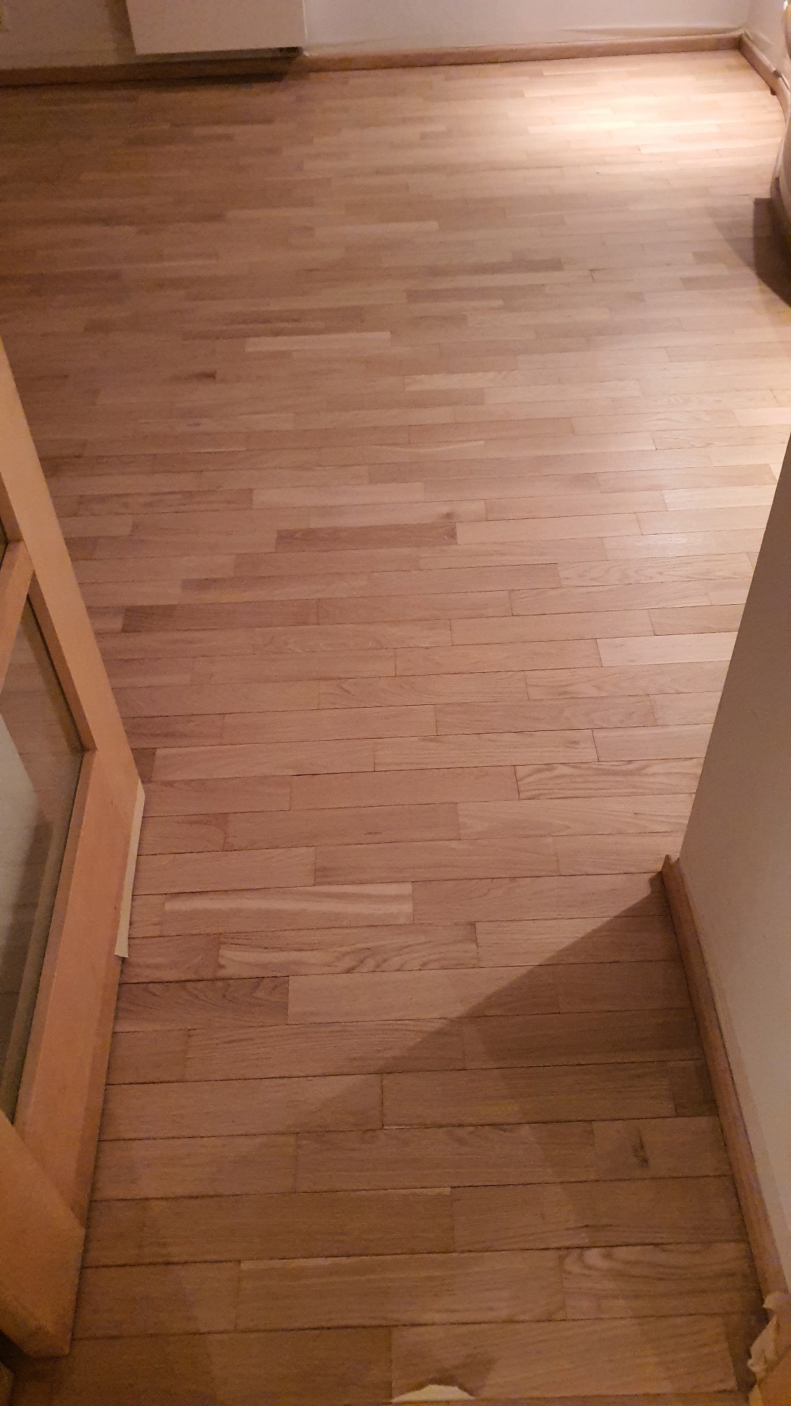 Parkiet po renowacji, widoczne świeżo wycyklinowane deski podłogowe z naturalnego drewna, jasny odcień, listwy przypodłogowe wzdłuż ściany.