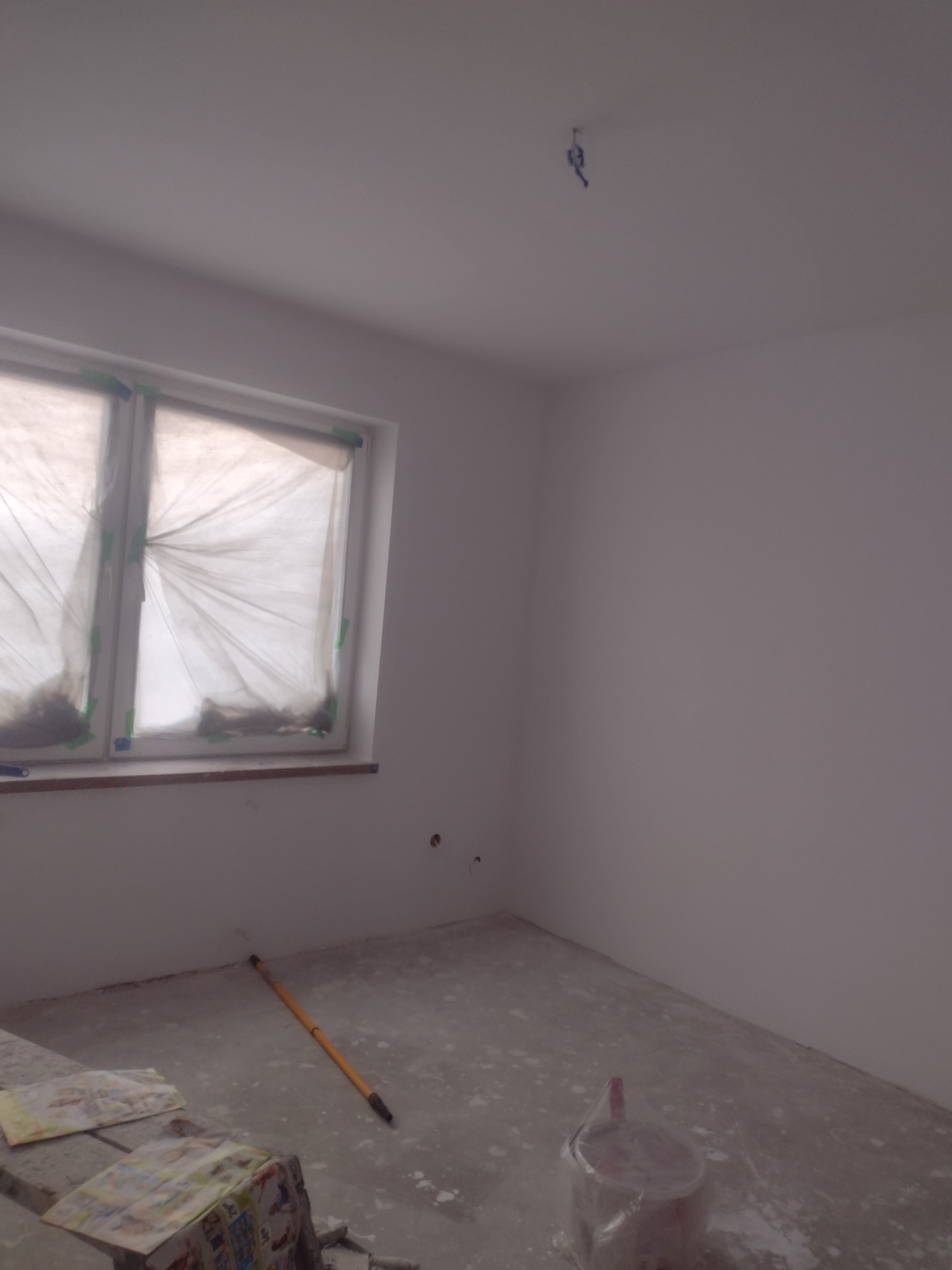 Przygotowane do malowania pomieszczenie w Radomsku, okna zabezpieczone folią, widoczny wałek malarski i wiadro farby.