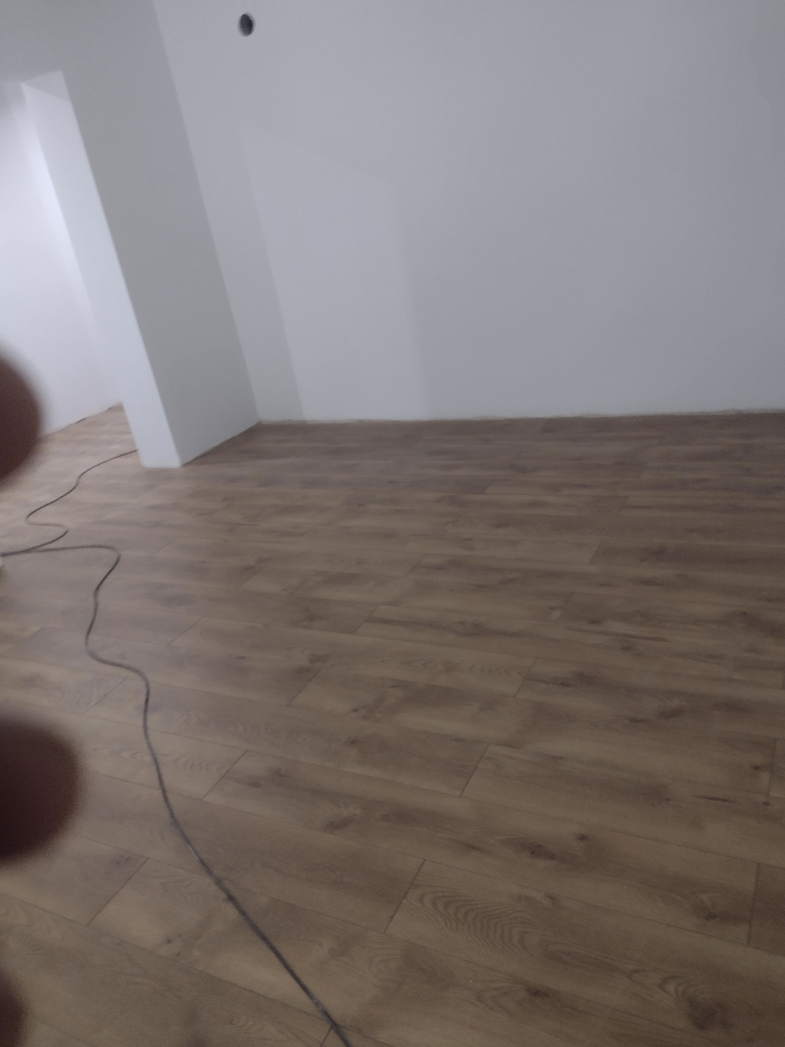 Ułożone panele podłogowe w nowym, jasnym pomieszczeniu z widocznym kablem na podłodze.