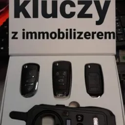 Kodowanie kluczy samochodowych z immobilizerem: trzy klucze i programator w białym pudełku na biurku.
