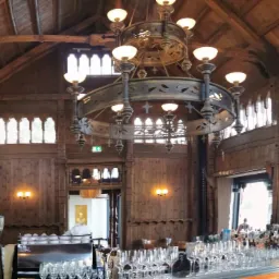 Wnętrze lokalu usługowego w Gdyni z drewnianą zabudową, ozdobnym żyrandolem i barem z licznymi kieliszkami.