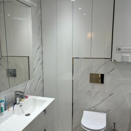 DREAM INTERIOR Elżbieta Chrupek - Nowoczesna, biała łazienka z marmurowymi płytkami, wiszącą toaletą i szafką pod umywalką, zintegrowana z wysoką szafą i wiszącym piecem gazowym.