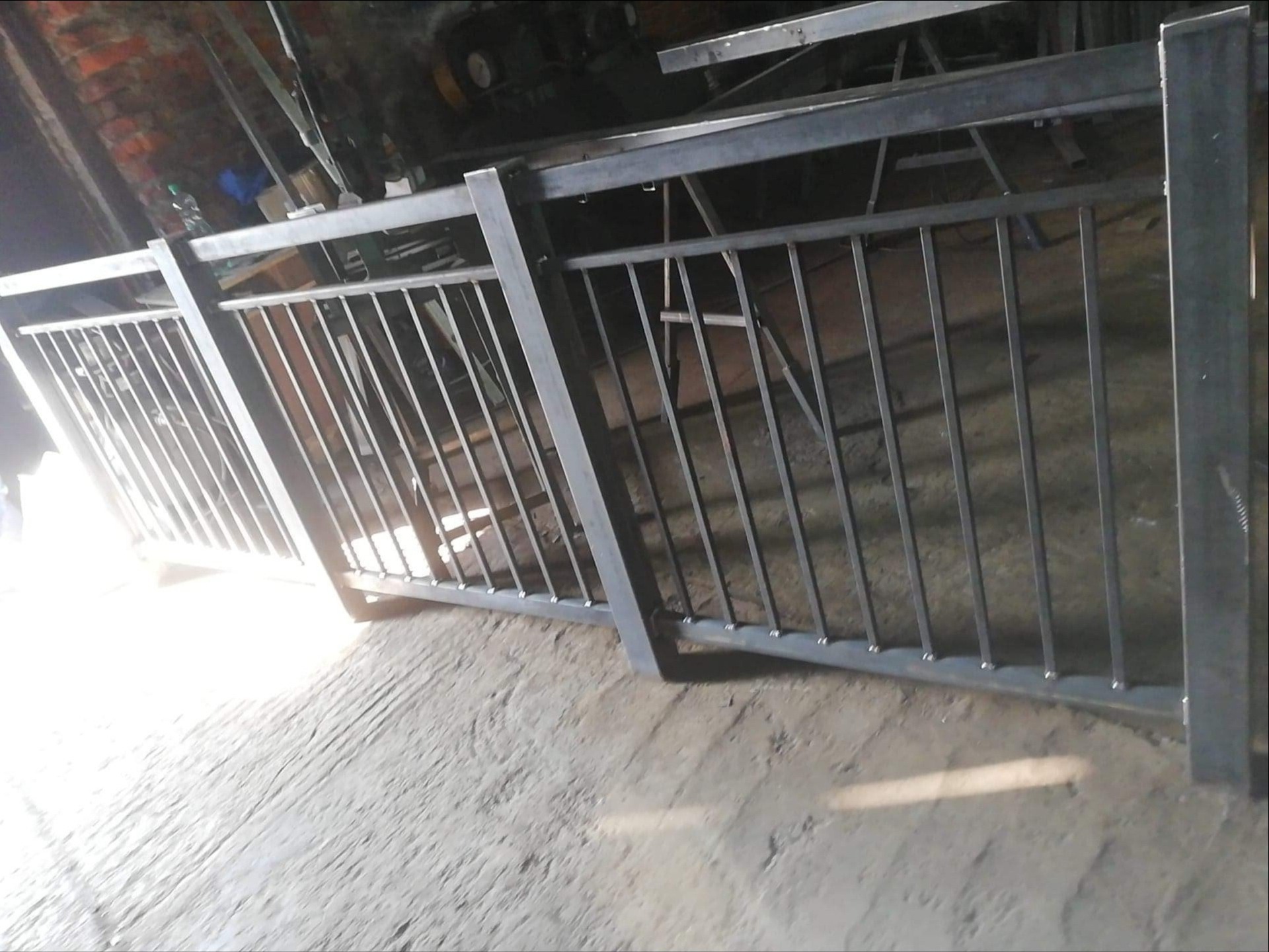 Surowa, metalowa konstrukcja balustrady z prętami, ustawiona w warsztacie, widoczne ślady spawania i niedoskonałości powierzchni.