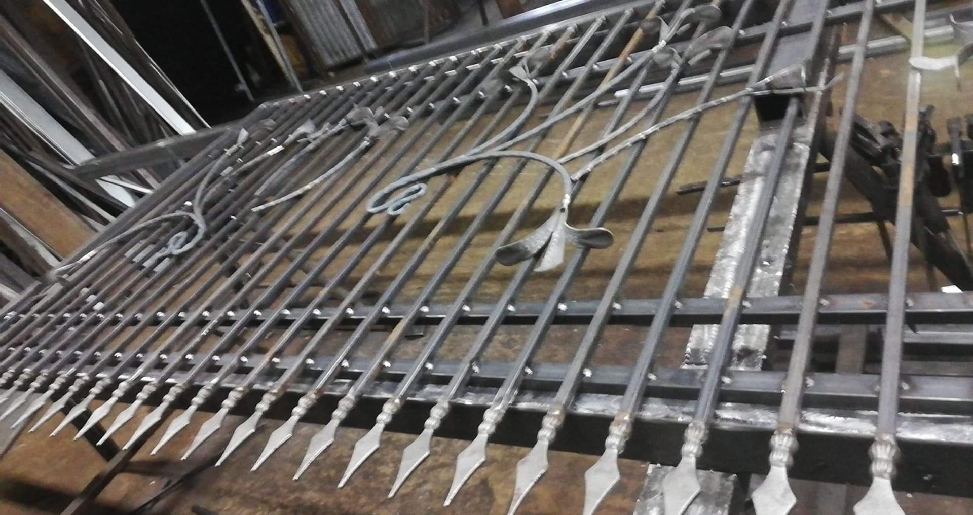 Surowy, metalowy element bramy z dekoracyjnym motywem roślinnym i grotami, w trakcie produkcji w warsztacie.