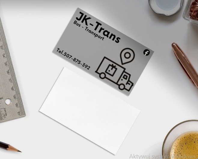 Wizytówka firmy transportowej JK-Trans z ikoną busa i pinezką lokalizacji, leżąca obok linijki, ołówka, długopisu, filiżanki kawy i pojemnika z biżuterią na białym tle biurka.