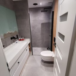 Fast Robert Wencel - Nowoczesna łazienka z szarą płytką, białą umywalką nablatową, czarną armaturą i kabiną prysznicową typu walk-in, widoczne tuby silikonu przy umywalce.