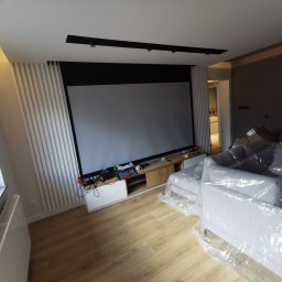 Fast Robert Wencel - Nowoczesny salon w Gdyni z dużym ekranem projekcyjnym, listwami dekoracyjnymi na ścianie i meblami zabezpieczonymi folią ochronną.
