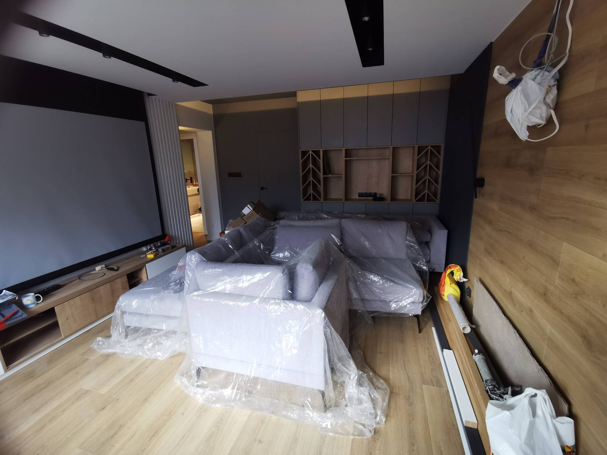 Salon w trakcie remontu: meble zabezpieczone folią ochronną, widoczne narzędzia i materiały budowlane, świeżo położona podłoga z paneli.