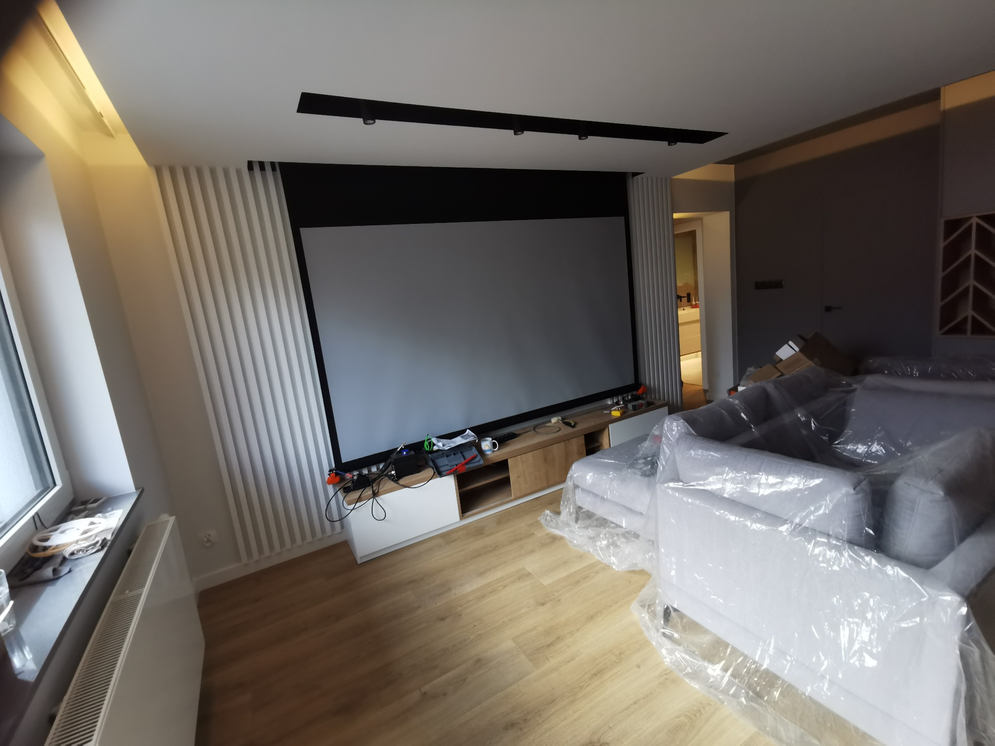 Nowoczesny salon w Gdyni z dużym ekranem projekcyjnym, listwami dekoracyjnymi na ścianie i meblami zabezpieczonymi folią ochronną.