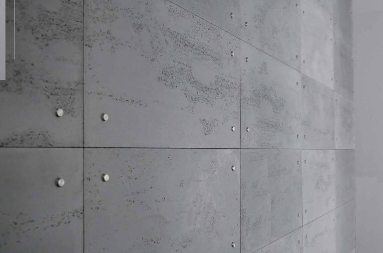 Szare panele ścienne z fakturą betonu, zamocowane za pomocą metalowych kołków, widoczne z boku, tworzące nowoczesną aranżację wnętrza.