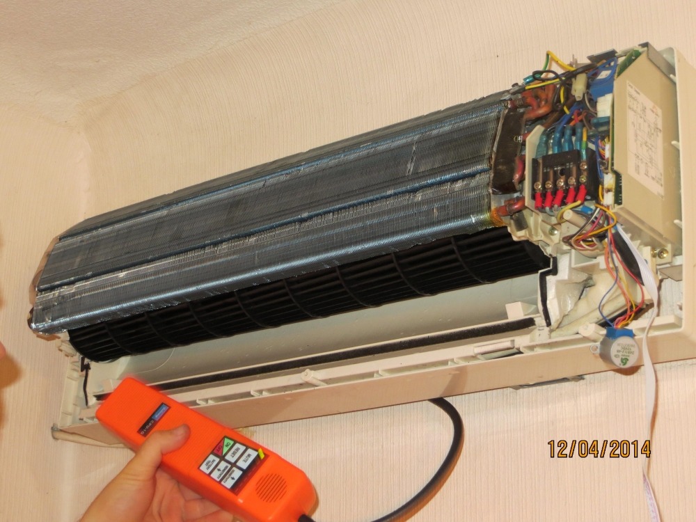 Otwarta jednostka wewnętrzna klimatyzacji podczas diagnostyki, widoczne żeberka chłodnicy, wentylator, okablowanie i tester w ręku serwisanta.