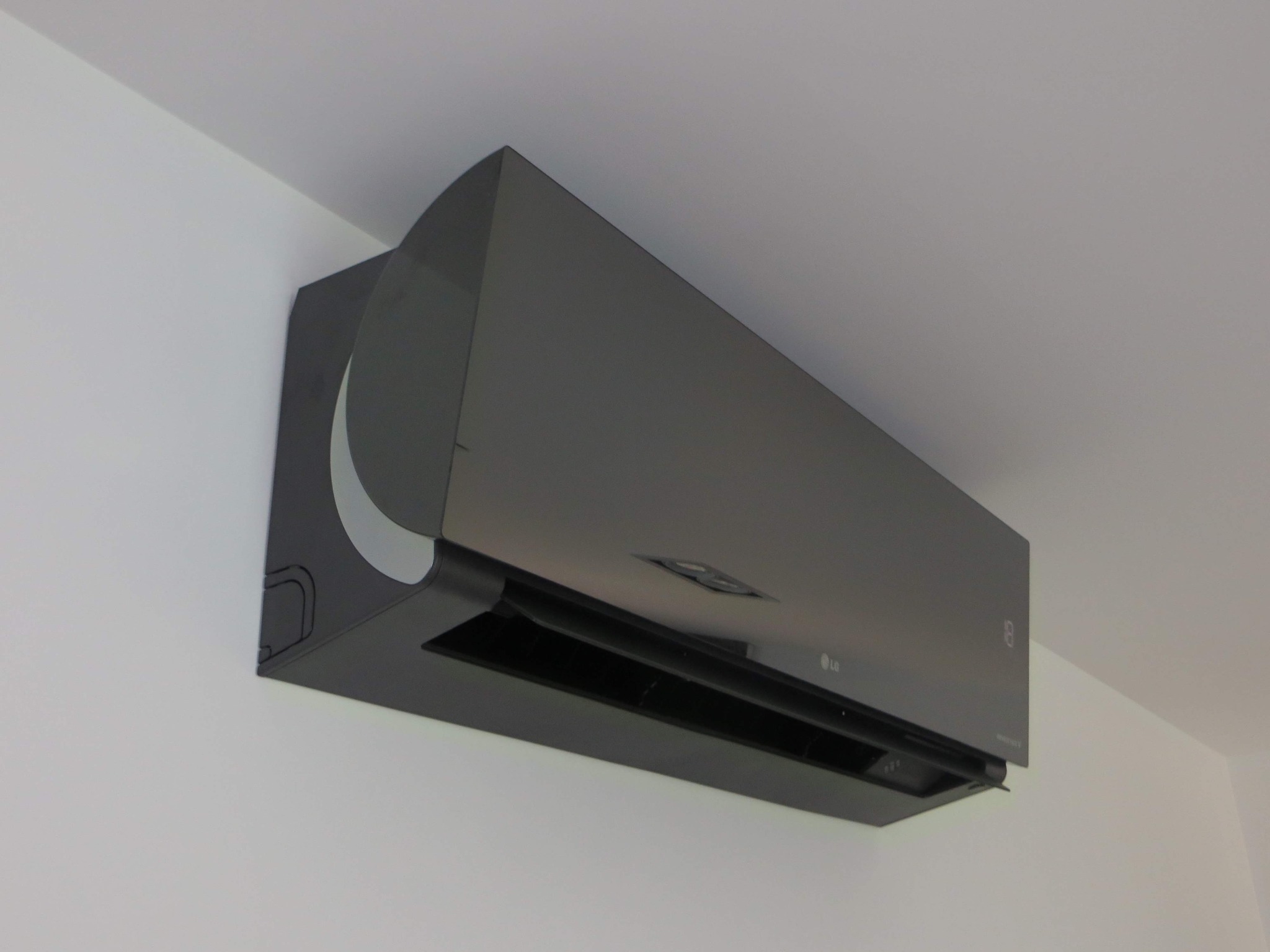 Czarny klimatyzator LG ARTCOOL Mirror zamontowany na białej ścianie, widoczny z boku pod kątem, z subtelnym odbiciem światła na obudowie.