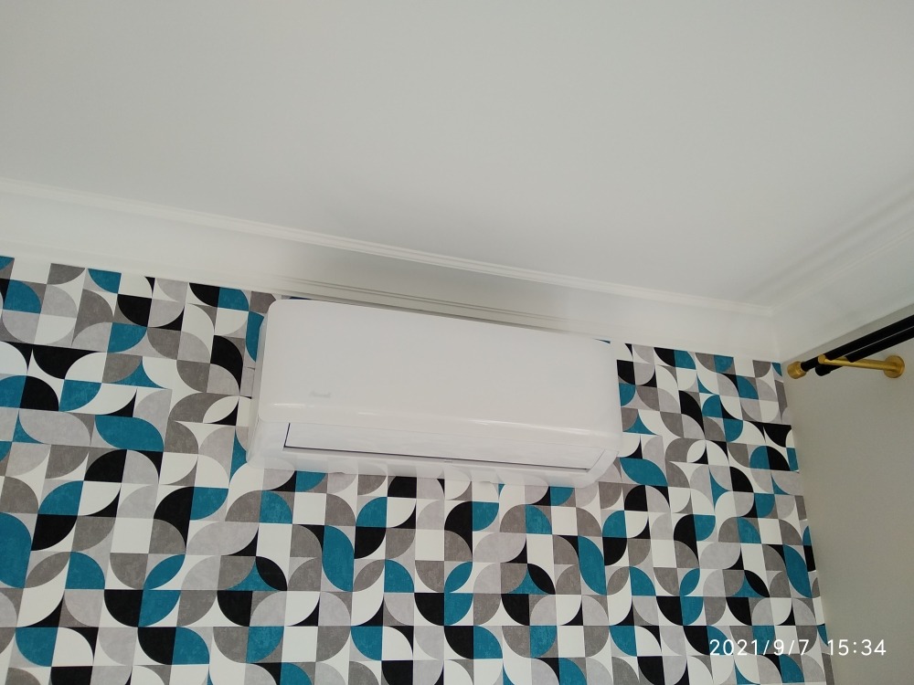 Biała jednostka klimatyzacji zamontowana na ścianie z wzorzystą tapetą w odcieniach błękitu, szarości i czerni, widok z dołu.