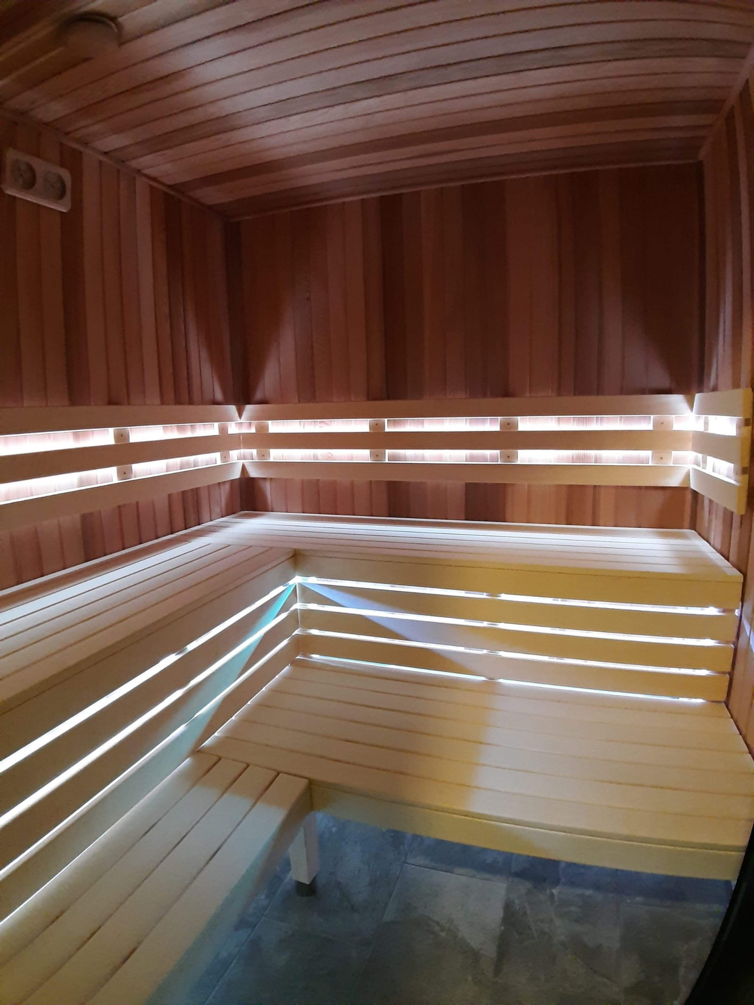 Wnętrze sauny wykończonej drewnem z podświetleniem LED zamontowanym za oparciami, widok na drewniane ławy i panele ścienne.