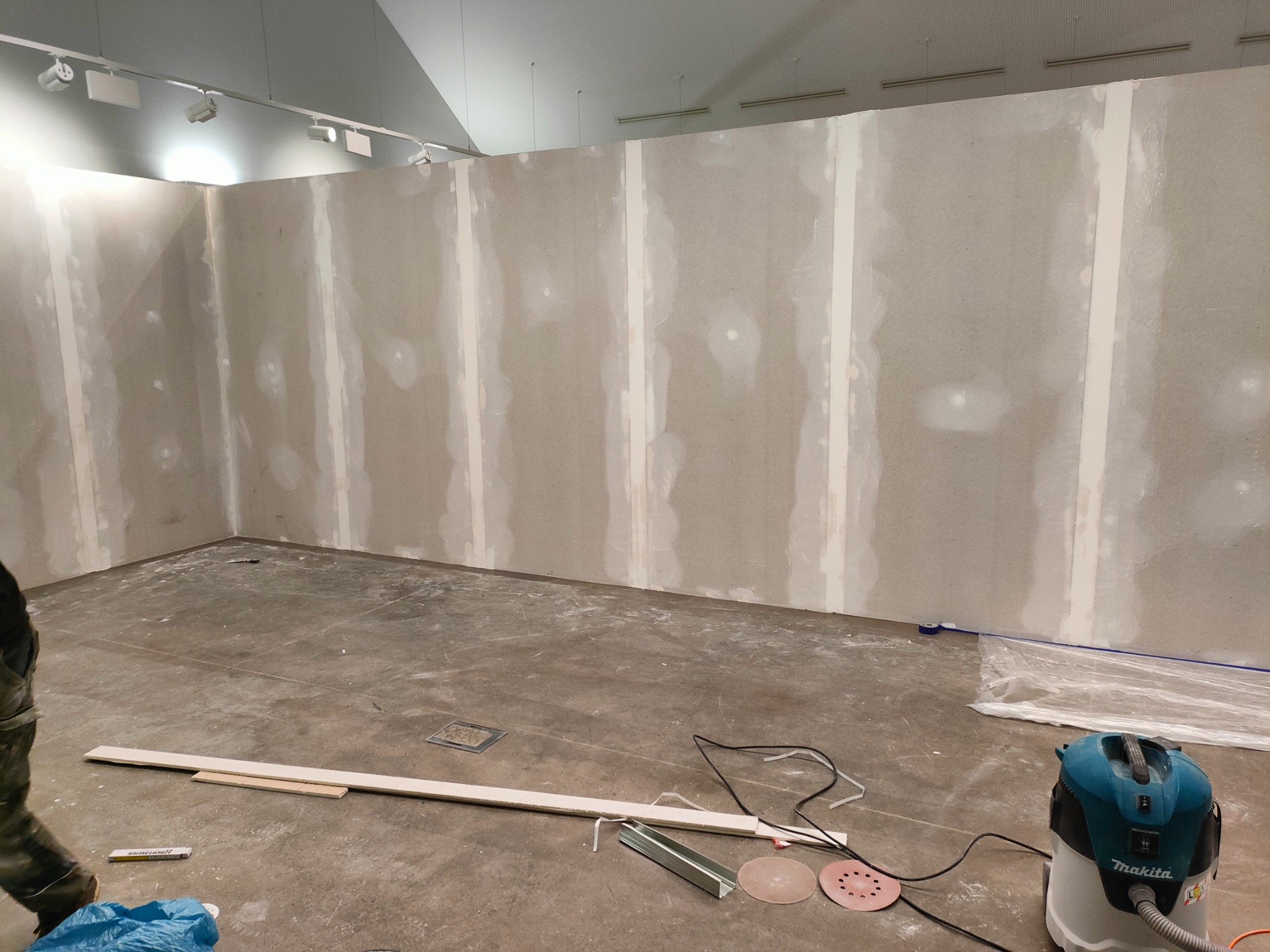 Wnętrze w trakcie prac wykończeniowych: ściany z płyt kartonowo-gipsowych z widocznymi łączeniami przed szpachlowaniem, na podłodze narzędzia, listwy przypodłogowe i odkurzacz przemysłowy Makita.
