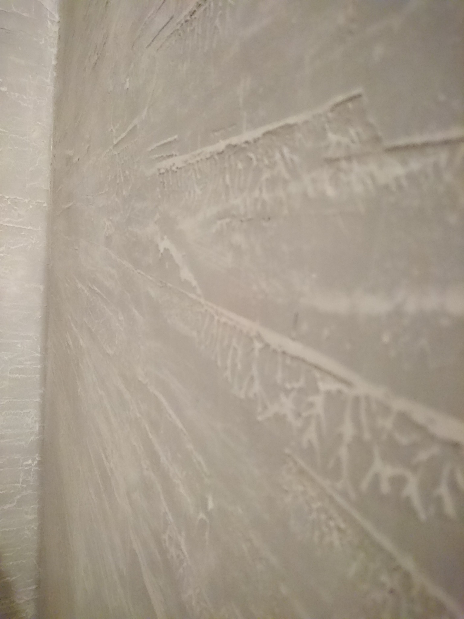 Szara ściana z dekoracyjną fakturą, imitującą pęknięcia i nierówności, widok z perspektywy narożnika pomieszczenia.