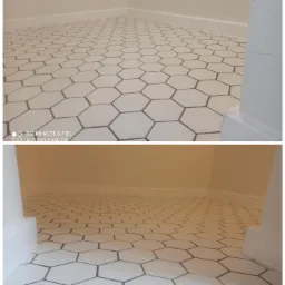 Ułożona podłoga w łazience z białych, heksagonalnych płytek z ciemnymi fugami, widok z niskiej perspektywy, z widocznymi przypodłogowymi listwami i fragmentem ościeżnicy.