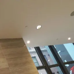 Sufit w biurze z wbudowanymi okrągłymi lampami i głośnikiem, widok z dołu na okno z widokiem na budynek.