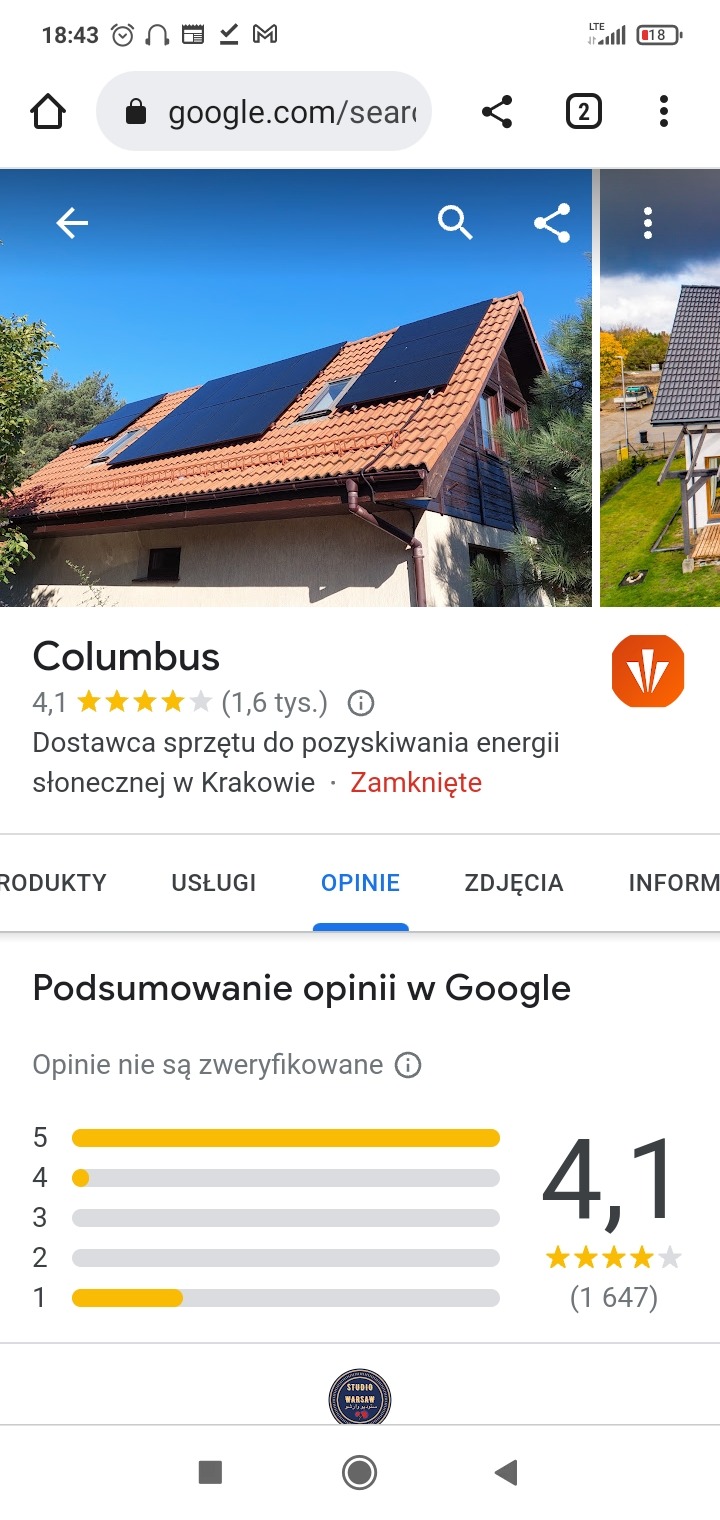 Panele fotowoltaiczne na skośnym dachu domu jednorodzinnego z czerwoną dachówką, widok z poziomu ziemi w słoneczny dzień.