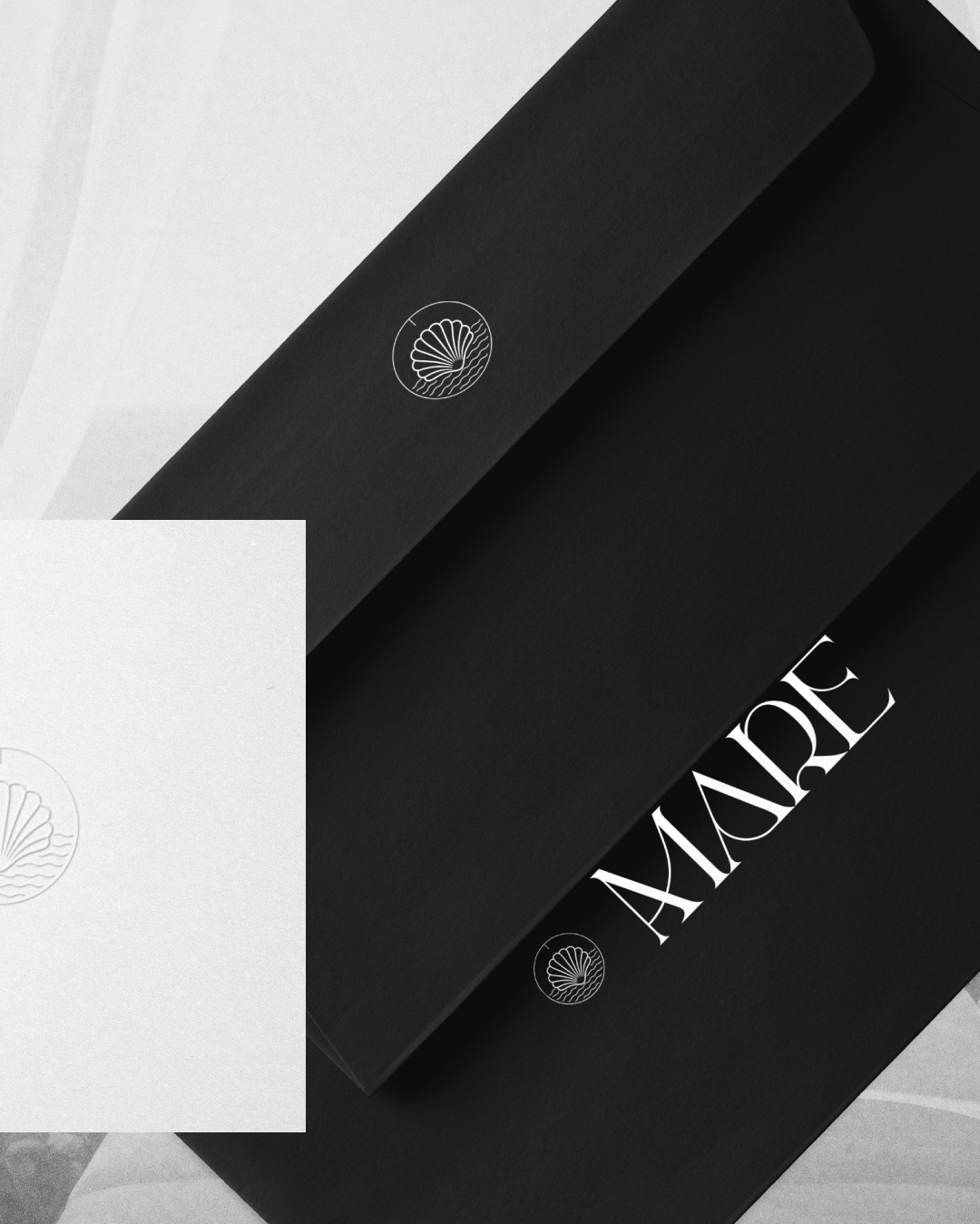 Eleganckie czarne koperty z białym logo muszli i napisem 'MARE' w minimalistycznym stylu, na jasnym tle.