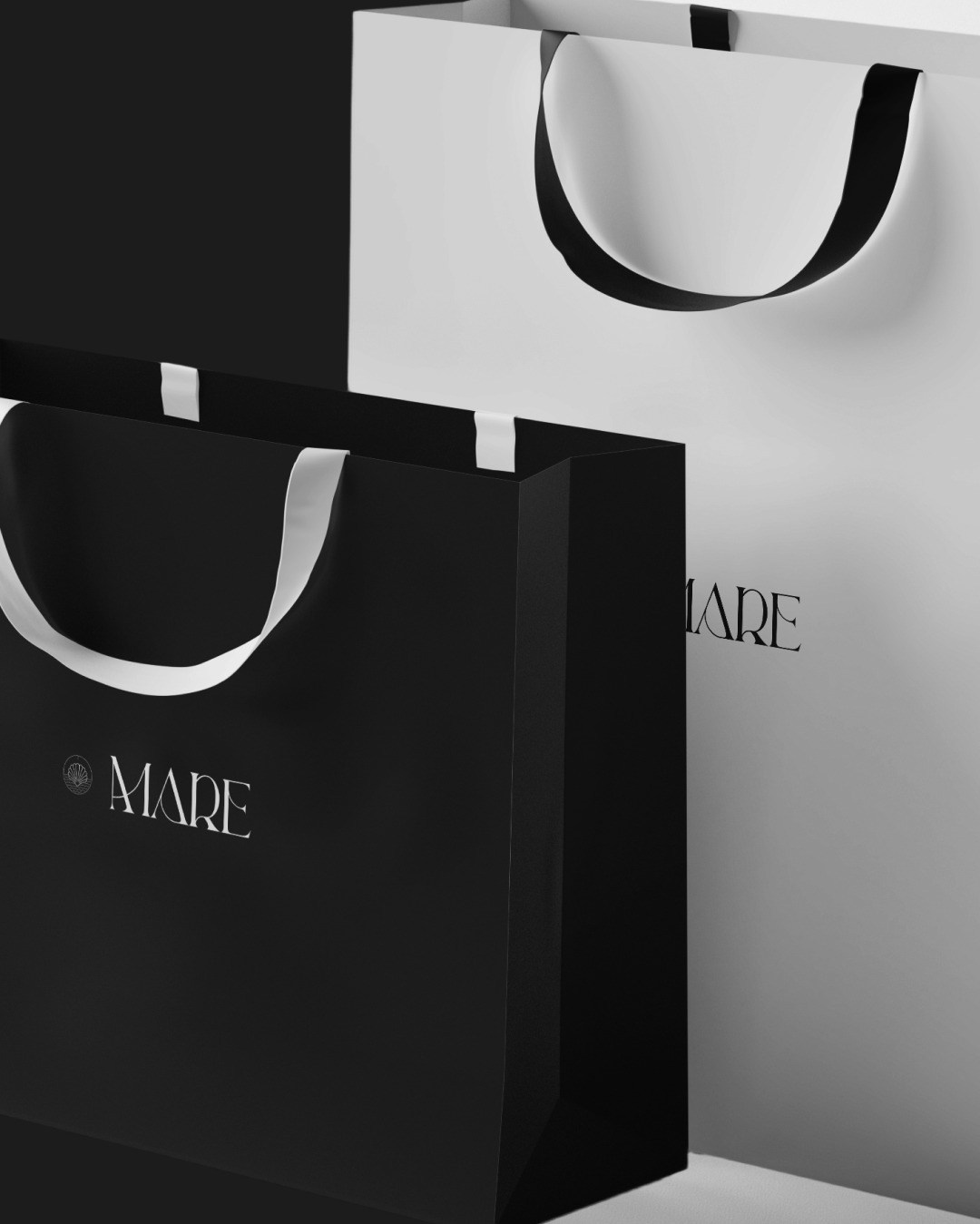 Dwie eleganckie torby papierowe w kolorze czarnym i białym z minimalistycznym logo 'MARE' w stylu retro, ustawione na jasnym tle.