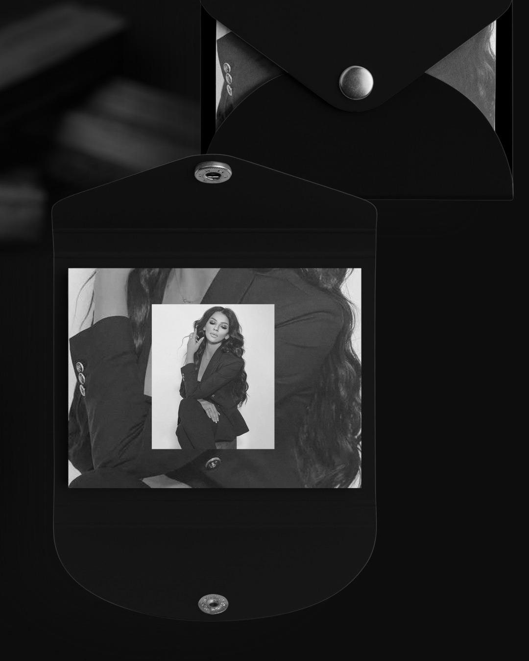 Czarno-białe zdjęcie portretowe kobiety w garniturze umieszczone wewnątrz czarnego, minimalistycznego etui zapinanego na zatrzask, z drugim etui widocznym w tle.