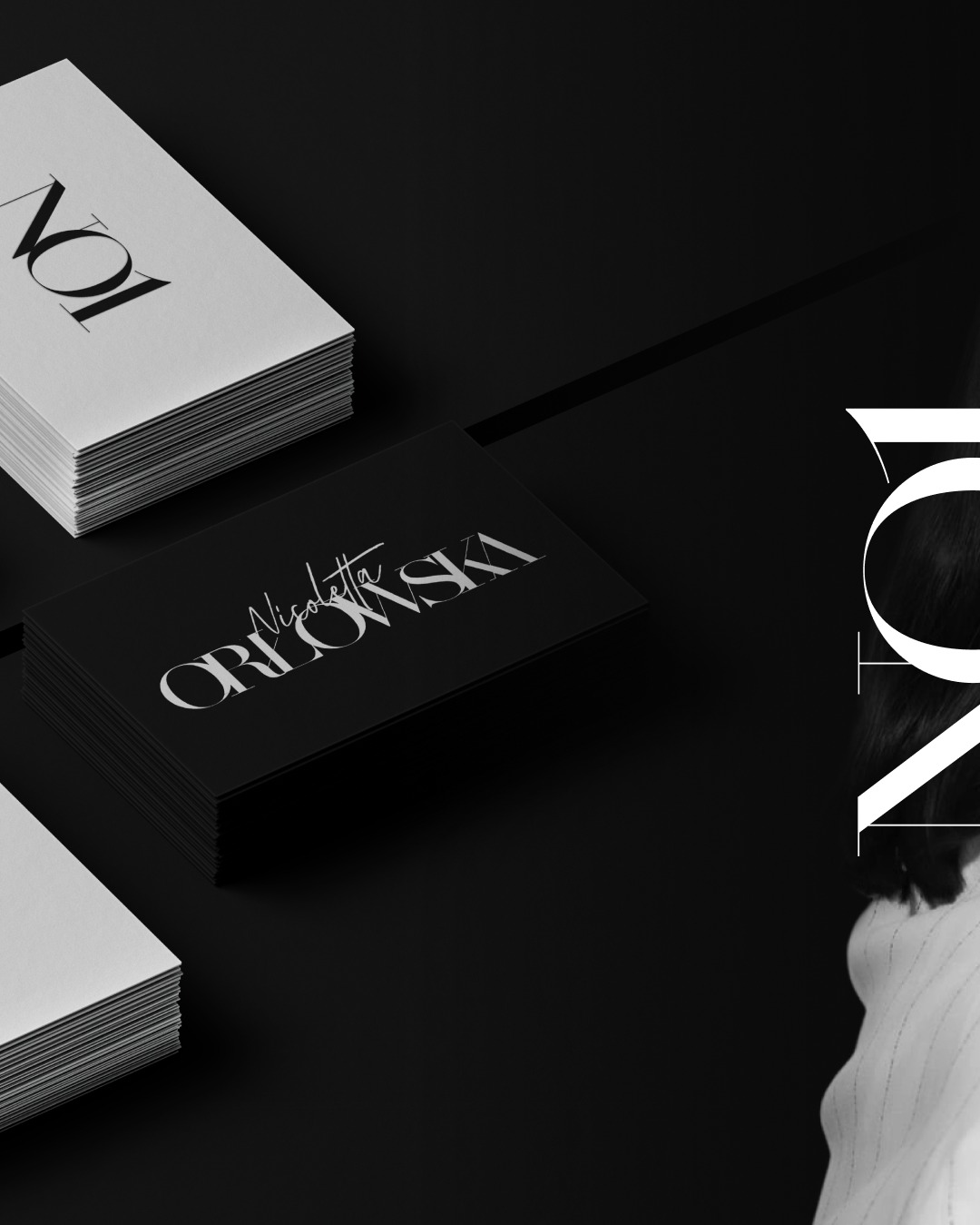 Stos wizytówek z eleganckim, kaligraficznym logo na czarnym tle, uzupełniony o stos białych wizytówek. Minimalistyczny design z elementami typografii.