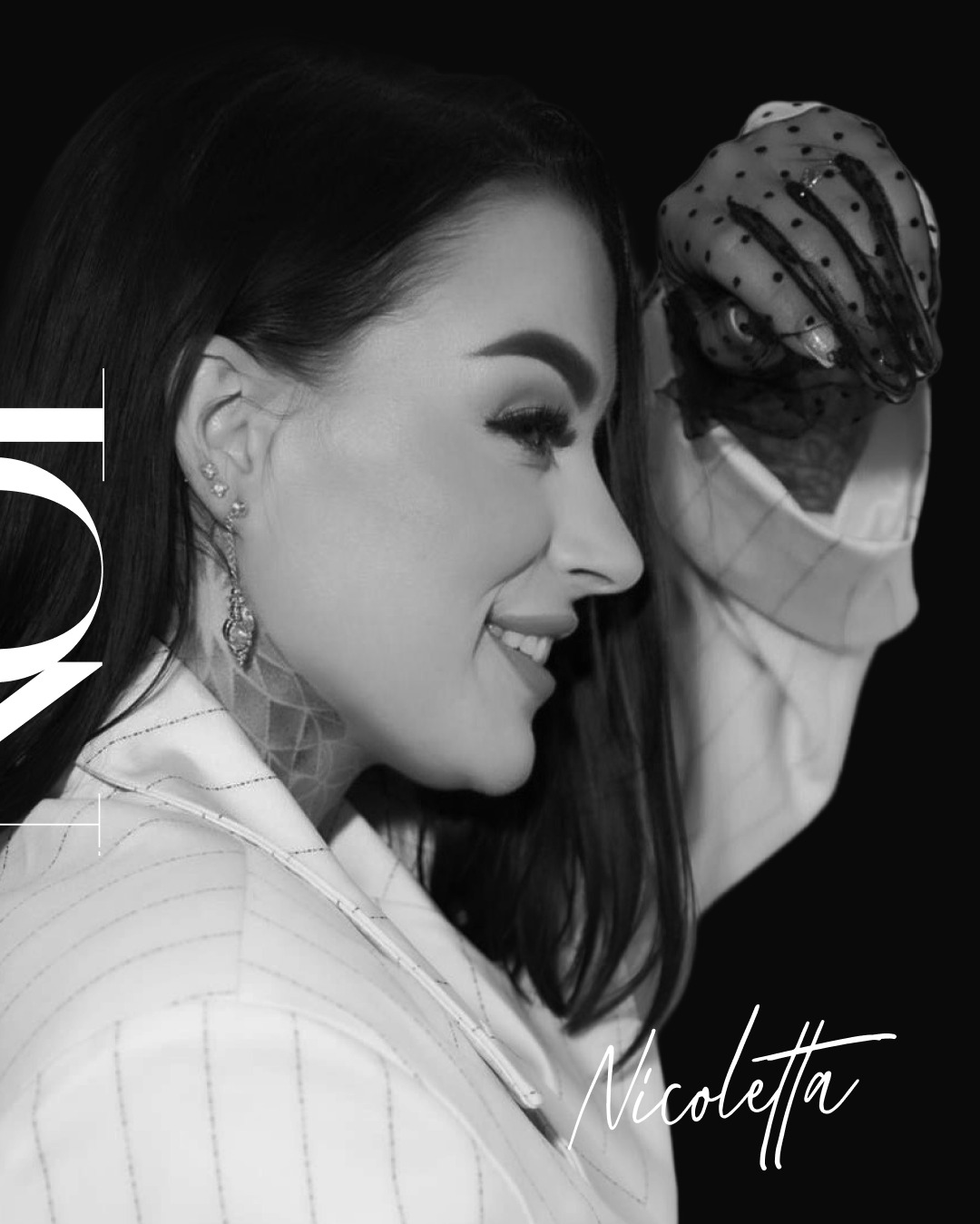 Czarno-biały portret kobiety z profilu, z delikatnym uśmiechem, w marynarce w paski, z widocznymi kolczykami i tatuażem na szyi. W tle ciemne tło i odręczny podpis.