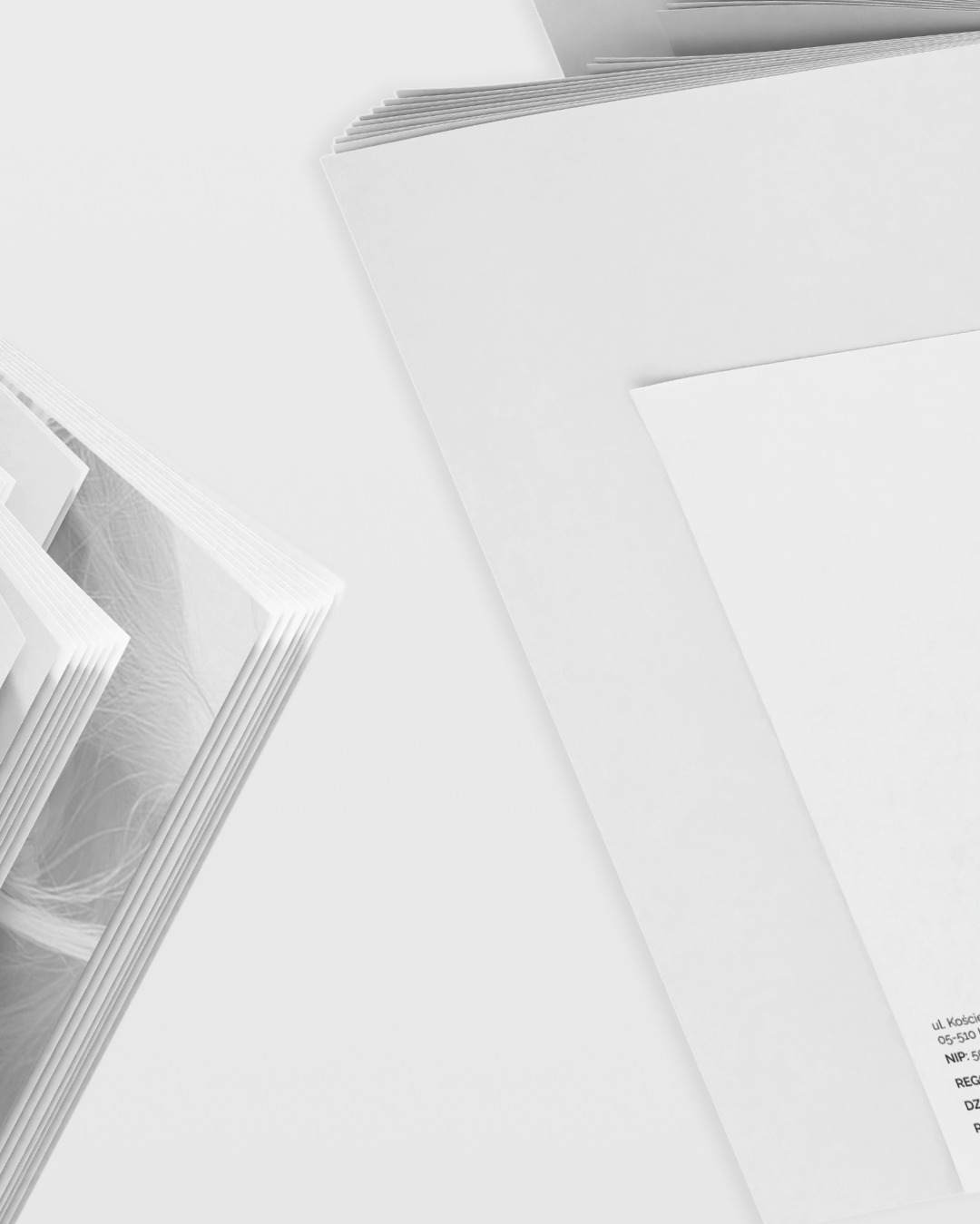 Stos białych kartek z delikatnym wzorem w lewym dolnym rogu i dane adresowe firmy z Gdańska w prawym dolnym rogu, na jasnym tle. Minimalistyczny design.