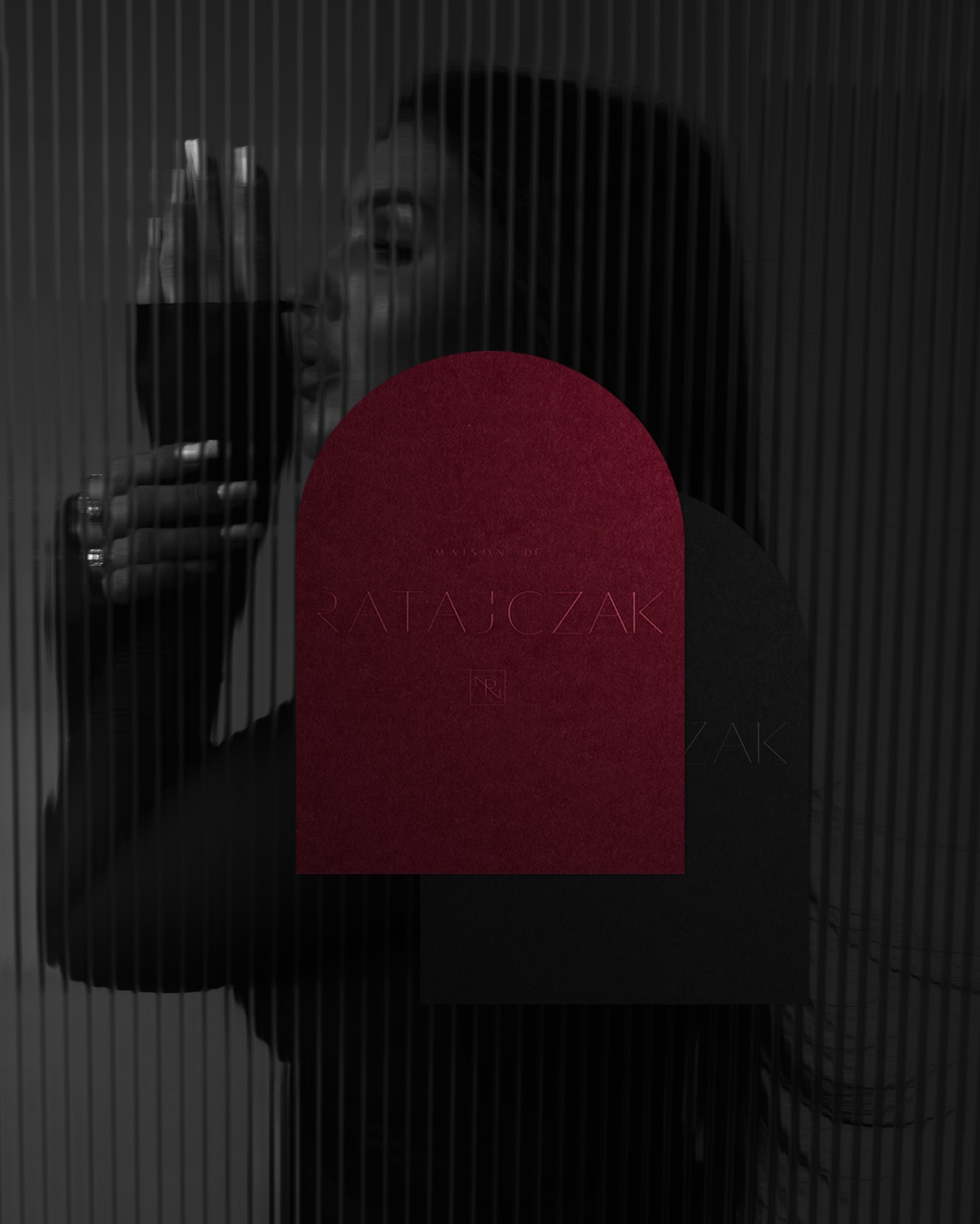 Wizytówka Maison De Ratajczak w odcieniach burgundu i czerni, z subtelnym tłoczeniem logo, na tle sylwetki kobiety z kieliszkiem wina, za szklaną ścianą.