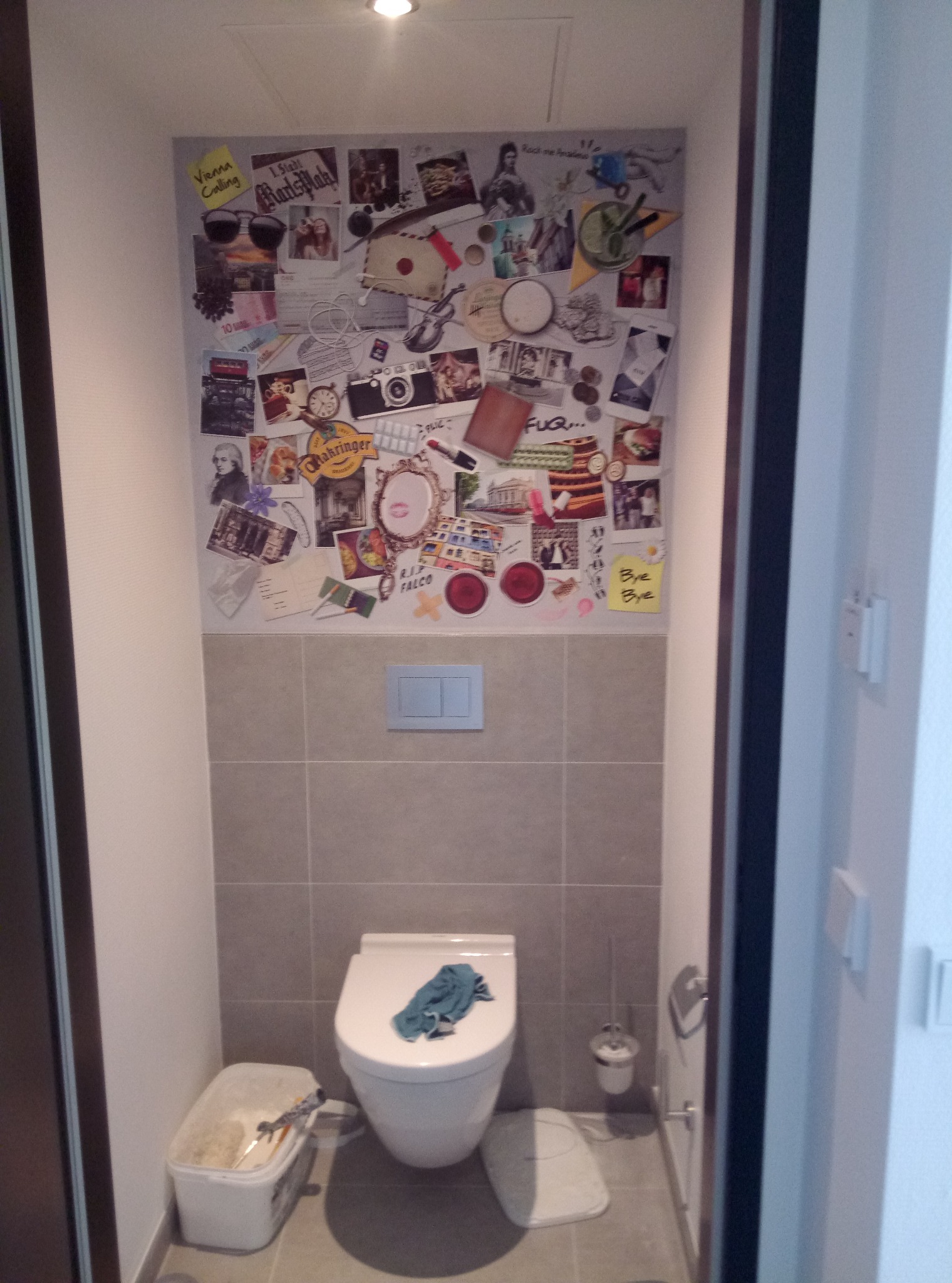 Kreatywna ściana w toalecie po remoncie w Pile, ozdobiona kolażem zdjęć i pamiątek, z widoczną szczotką do WC i pojemnikiem na narzędzia malarskie, sugerującym niedawne prace wykończeniowe.