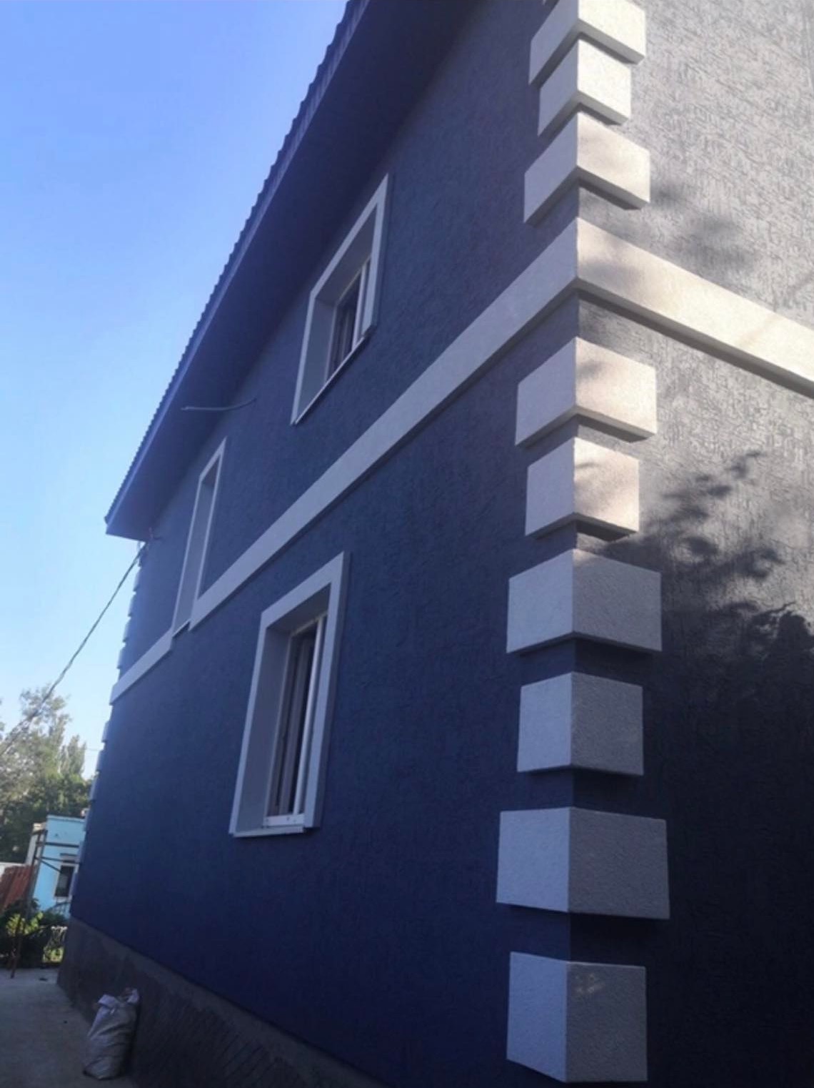 Niebieska elewacja domu z dekoracyjnymi białymi elementami narożnymi i obramowaniami okien, widok z dołu w słoneczny dzień.