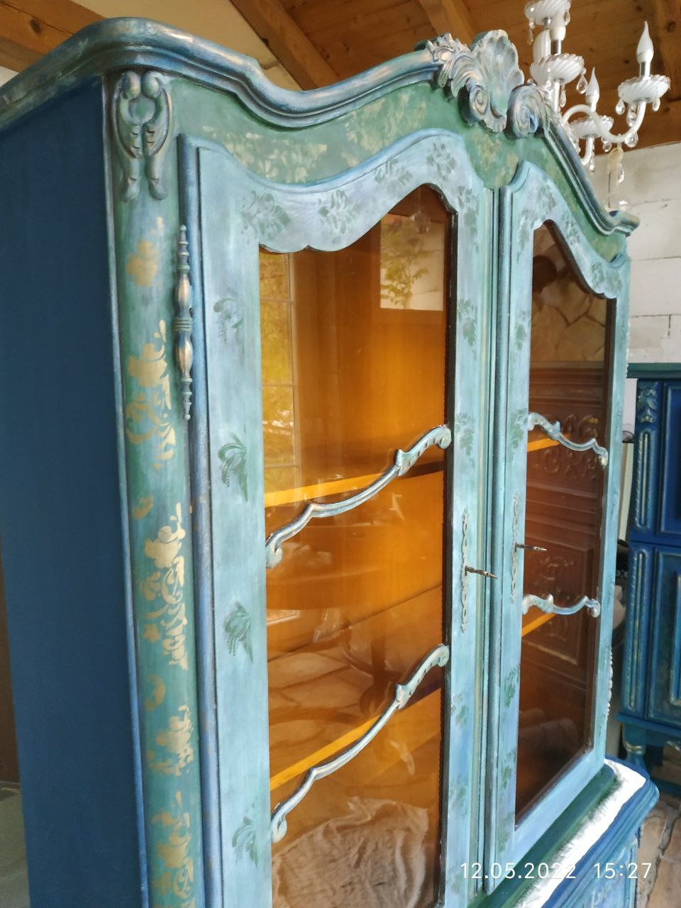 Odrestaurowana witryna w stylu vintage, pomalowana na niebiesko i turkusowo ze złotymi zdobieniami, przeszklone drzwi z charakterystycznymi uchwytami, widoczny fragment sufitu z lampą.